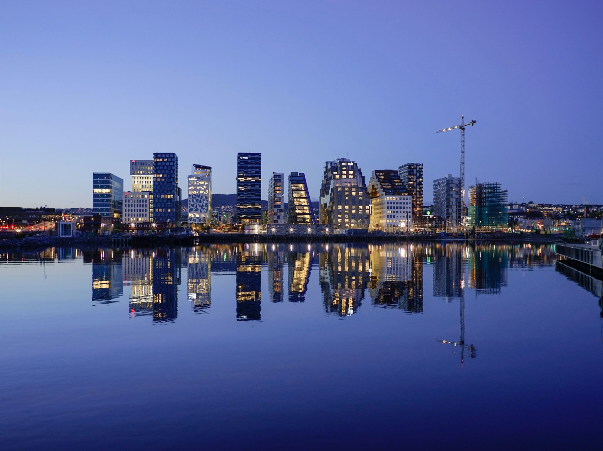 Nighttime view of Oslo, Norway, with modern buildings reflecting in calm water.