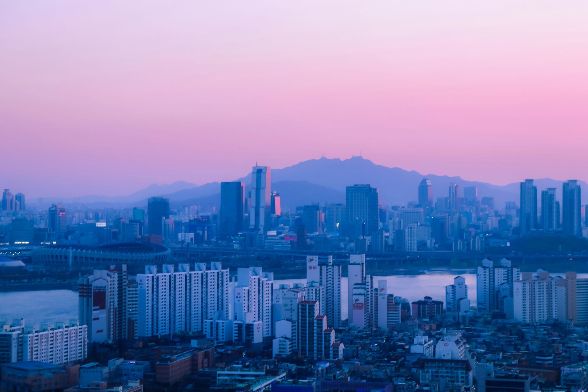 Seoul skyline at dusk with purple and blue hues; mountains in the background in South Korea.