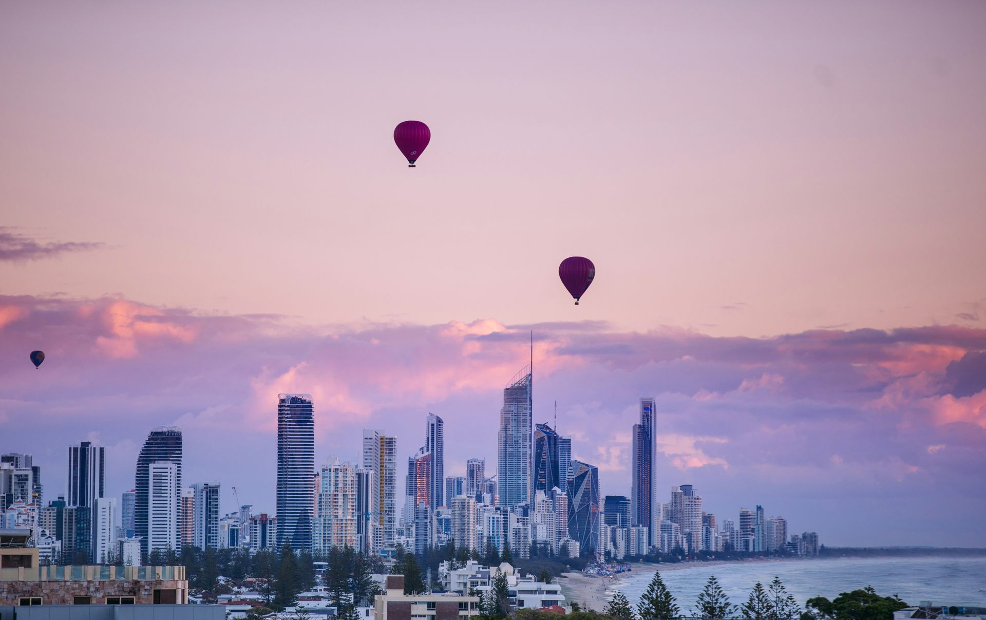 Two hot air balloons are flying over Gold Coast city at sunset in Australia.
