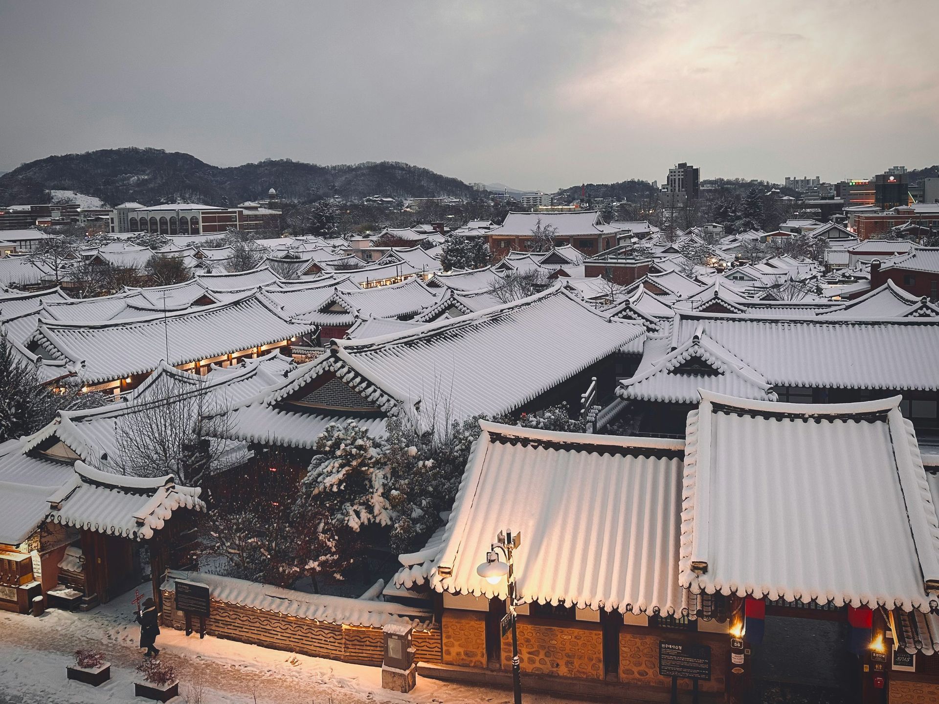 Snow-covered rooftops of traditional Korean houses with a mountain backdrop in Jeonju Hanok, South Korea.