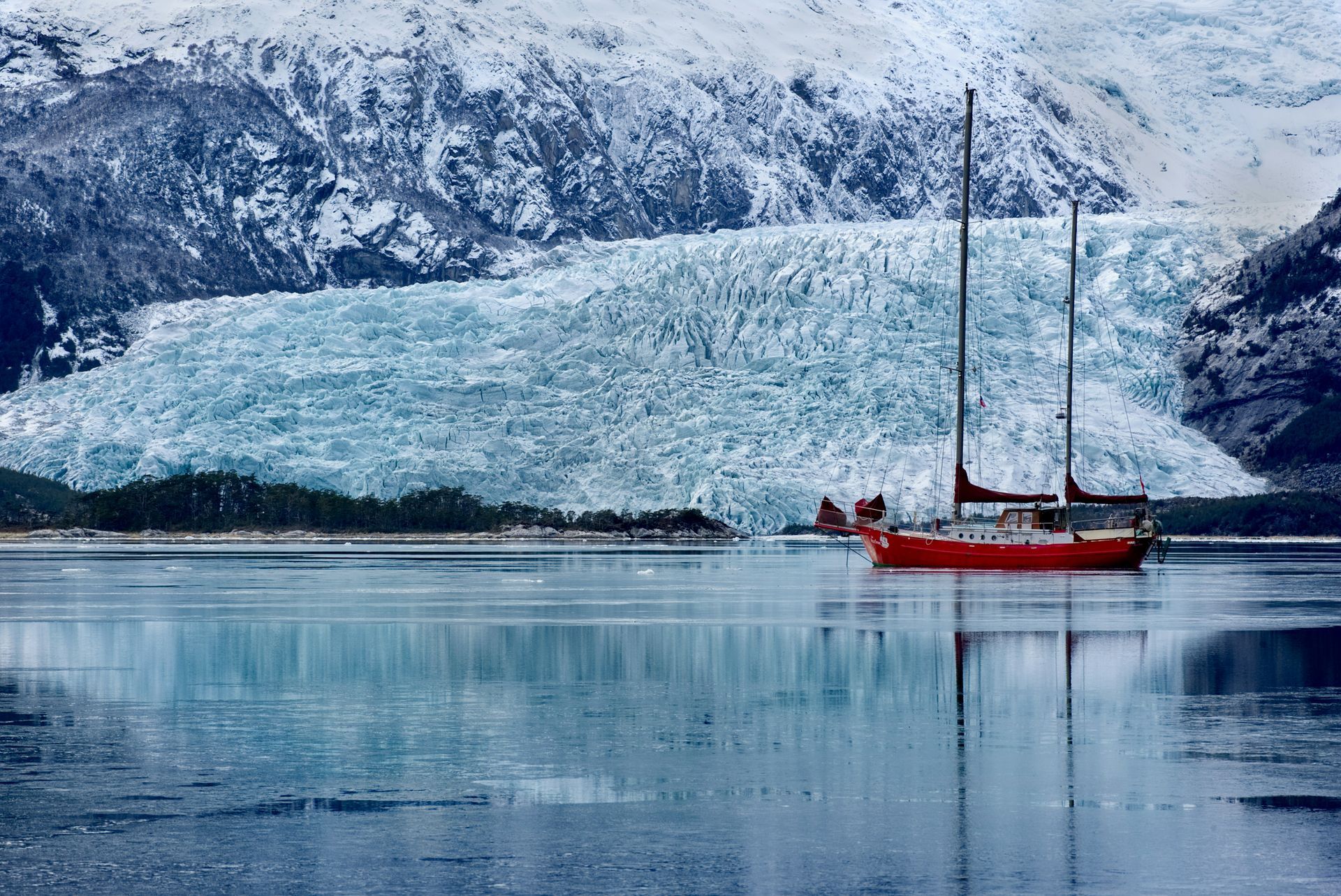Red sailboat in a glacial bay, ice and snow-covered mountains in the background in Aysén, Chile.