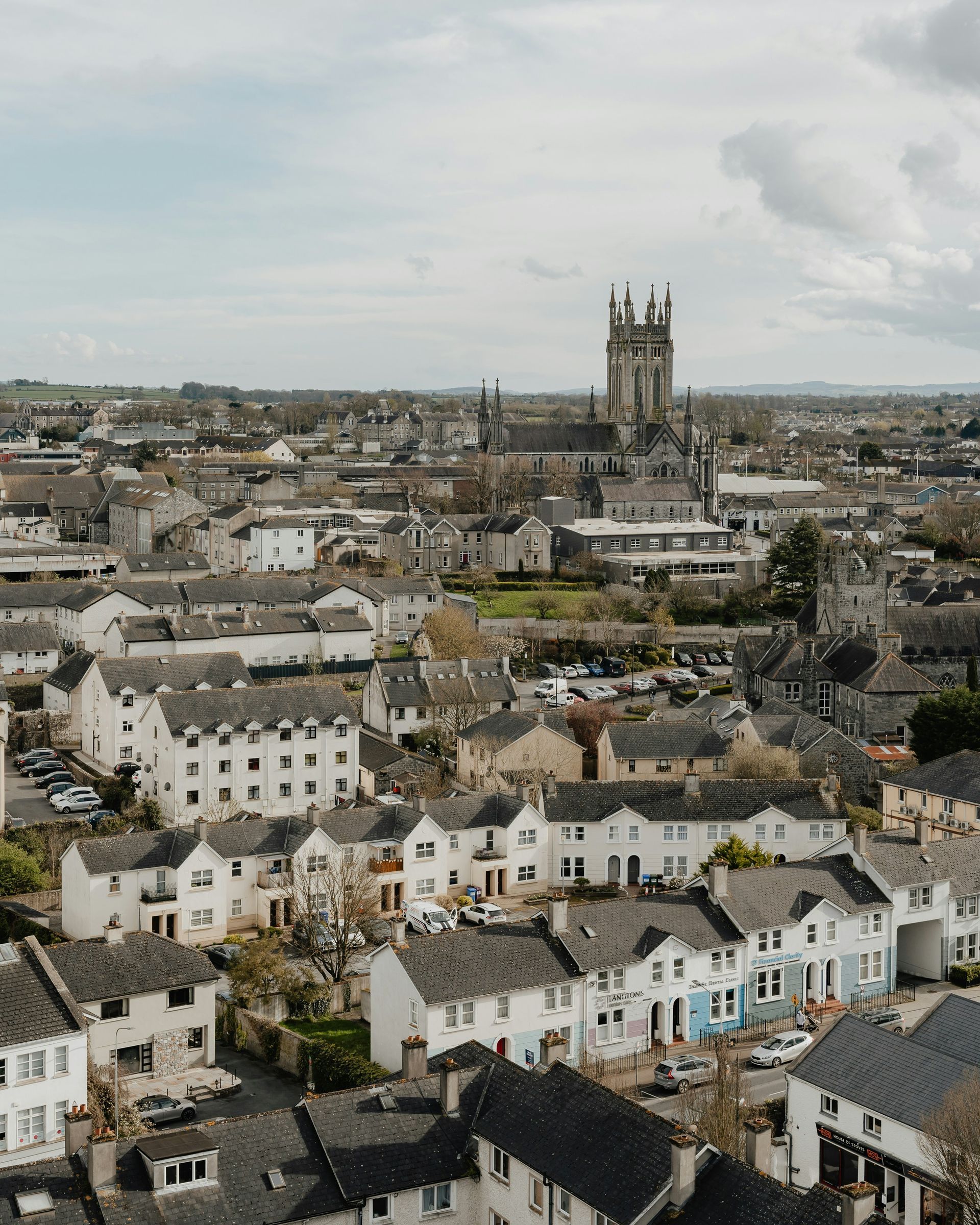 Aerial view of a town with a prominent cathedral, overcast sky, and rows of white houses in Kilkenny, Ireland.