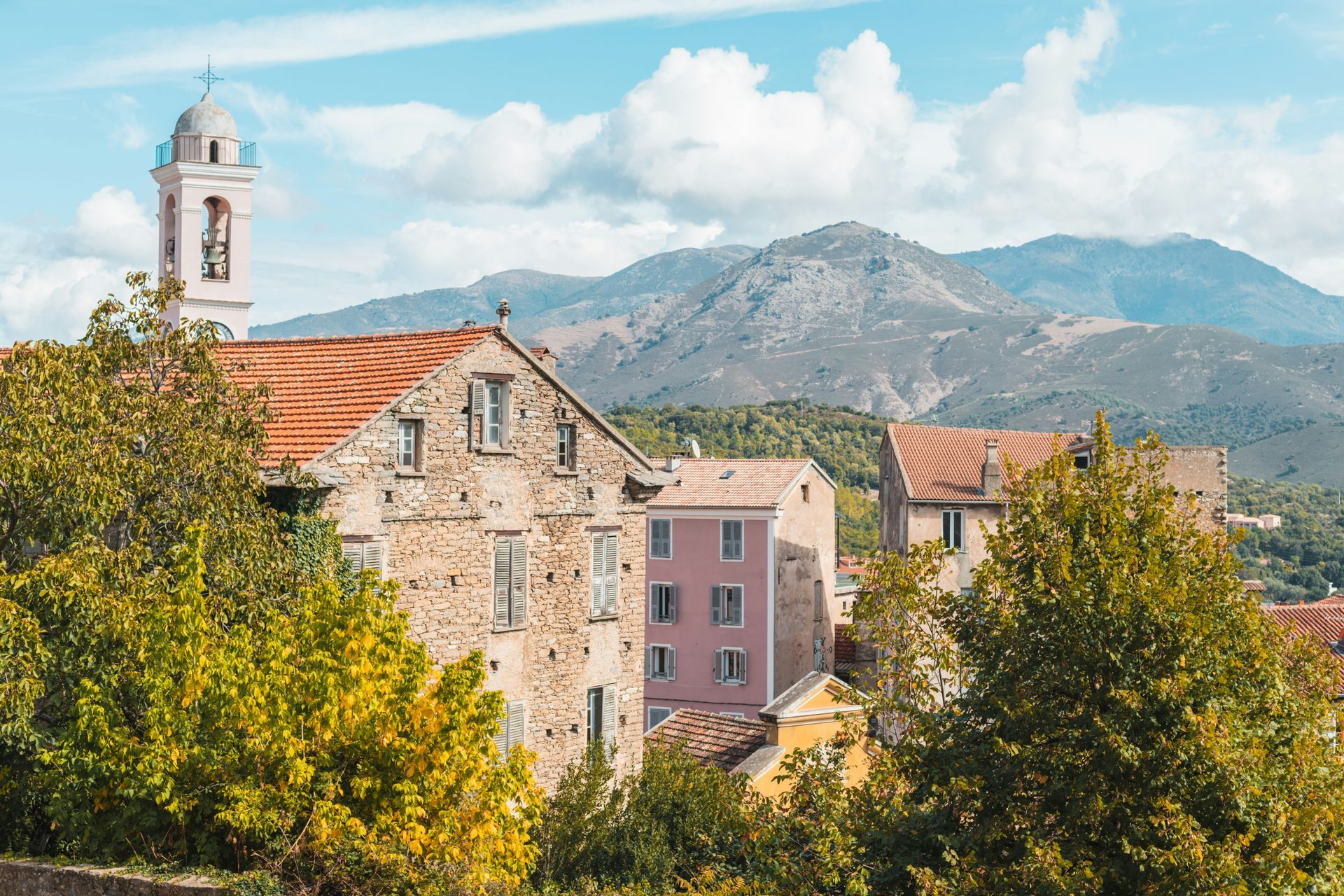 A small town with a bell tower and mountains in the background in Corsica, France.