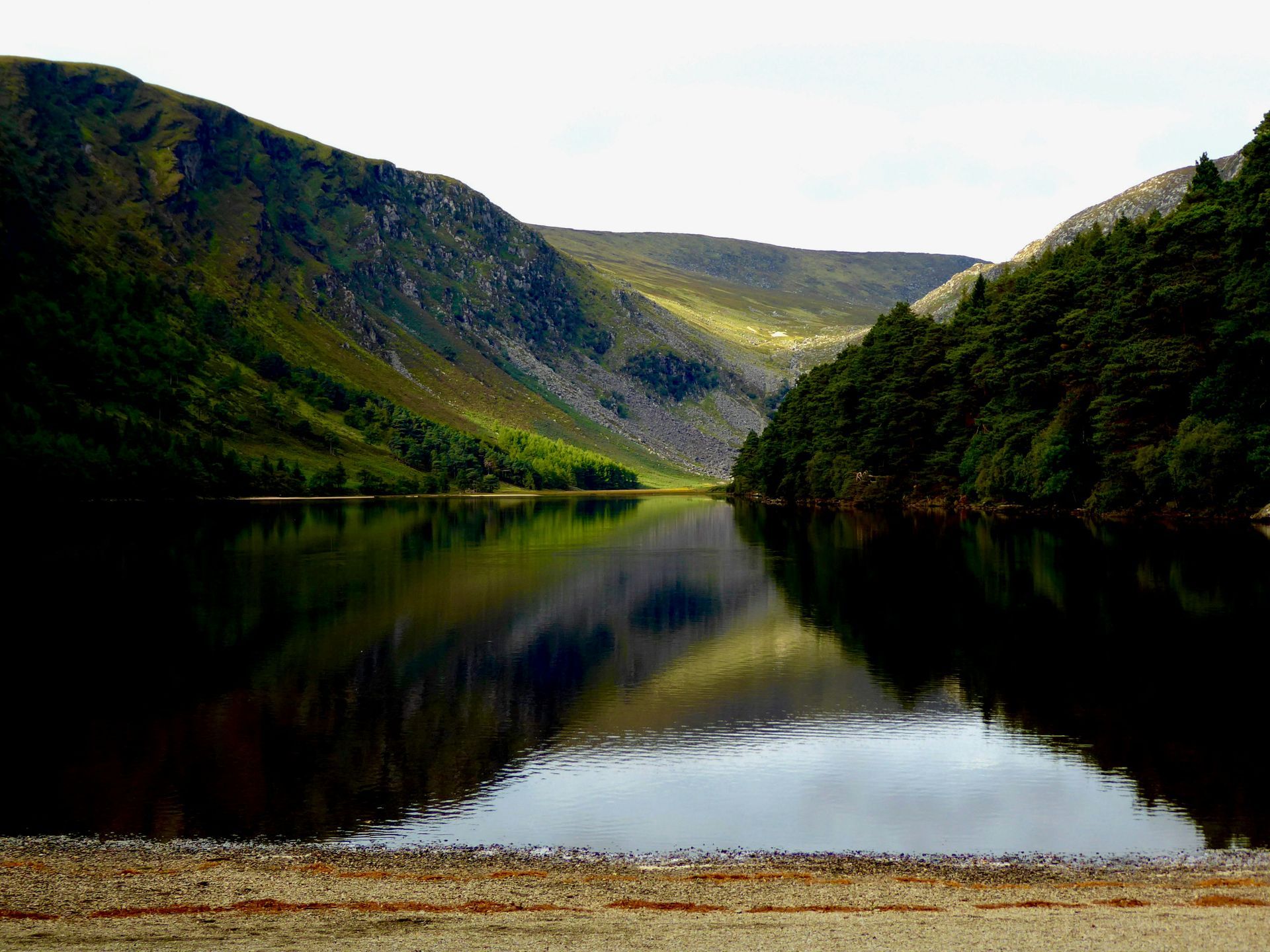A scenic lake nestled between green mountains, reflecting the surrounding landscape in Glendalough, Ireland.