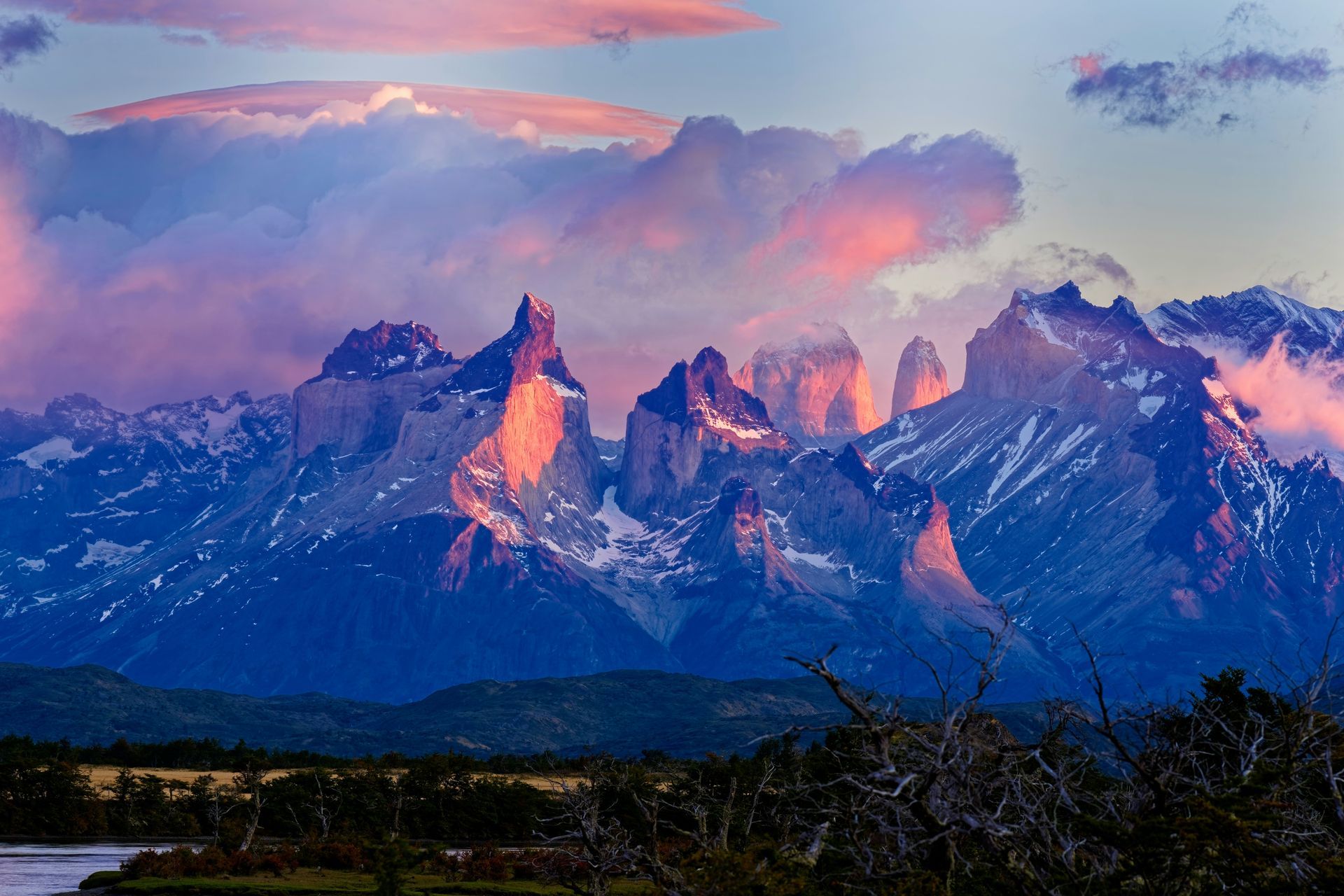 Snow-capped mountains at sunset with pink and orange clouds over the peaks in Torres del Paine, Chile.