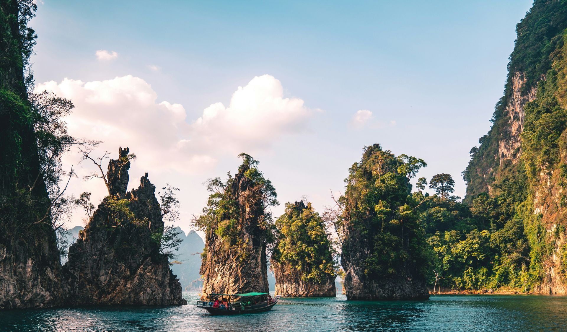 A boat is floating on a lake surrounded by mountains in Khao Sok National Park. Thailand.
