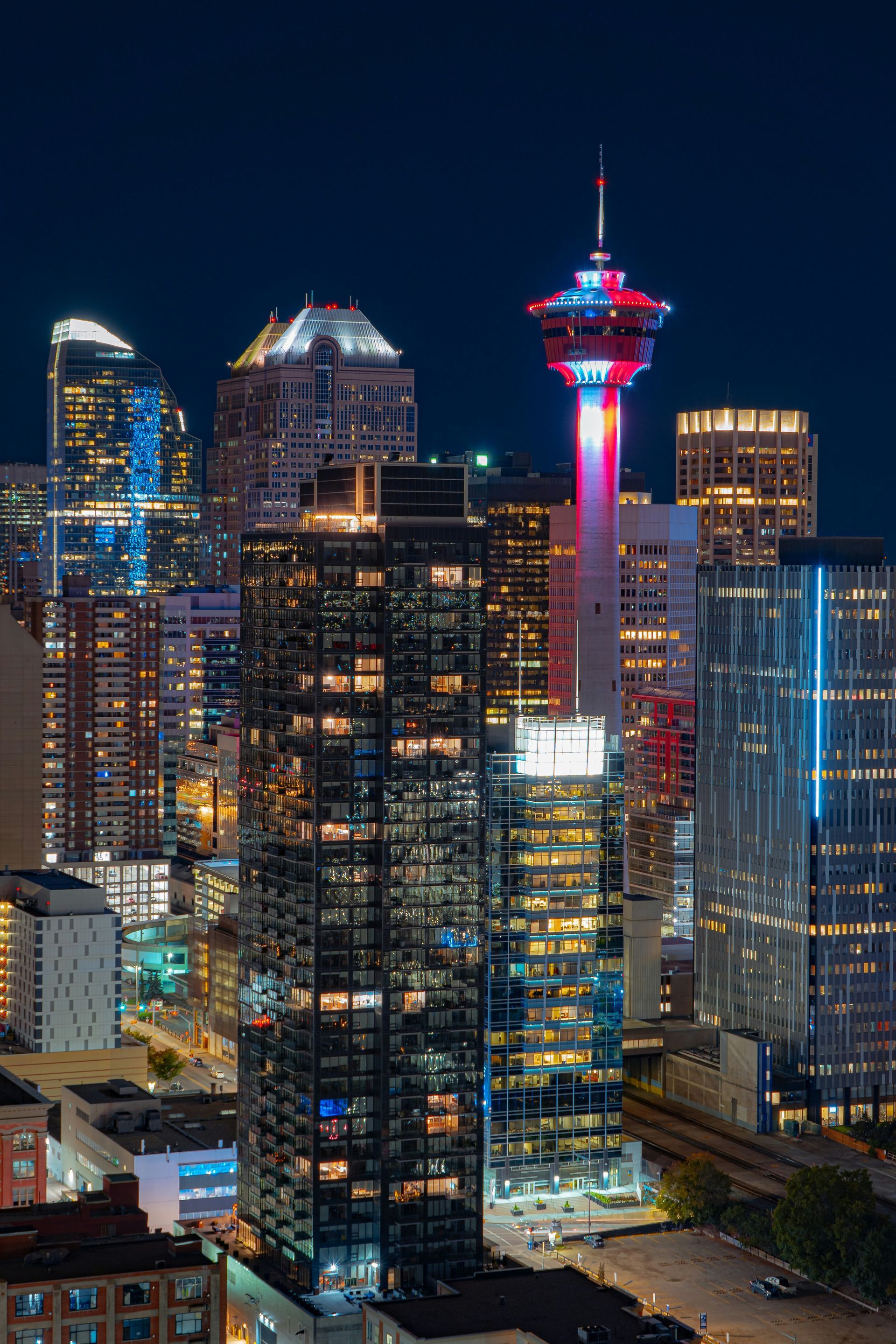 Nighttime view of Calgary's skyline, with the illuminated Calgary Tower as the focal point. Buildings display bright lights against a dark blue sky.