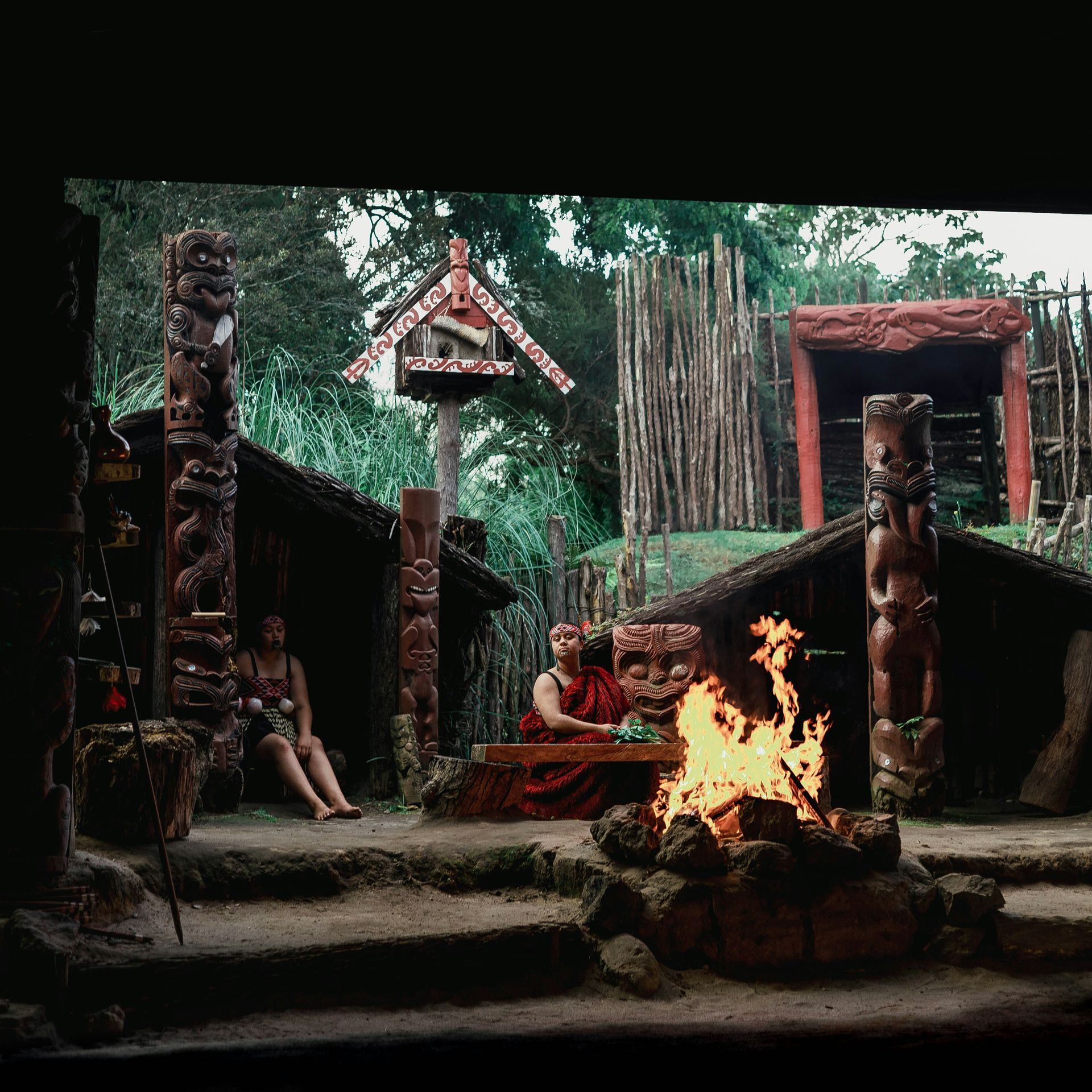 A group of people sitting around a fire in front of a totem pole in New Zealand.