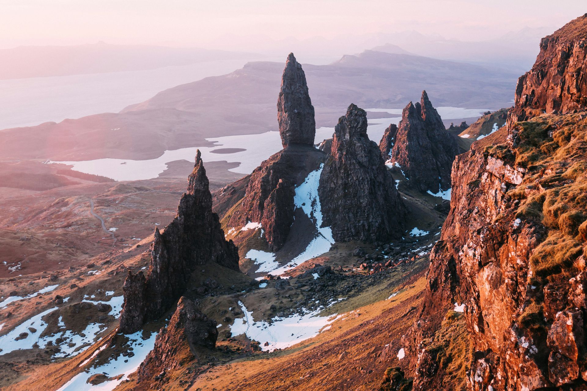 The Storr's jagged peaks on a mountainside with snow patches, overlooking a lake at dusk on the Isle of Skye, Scotland.