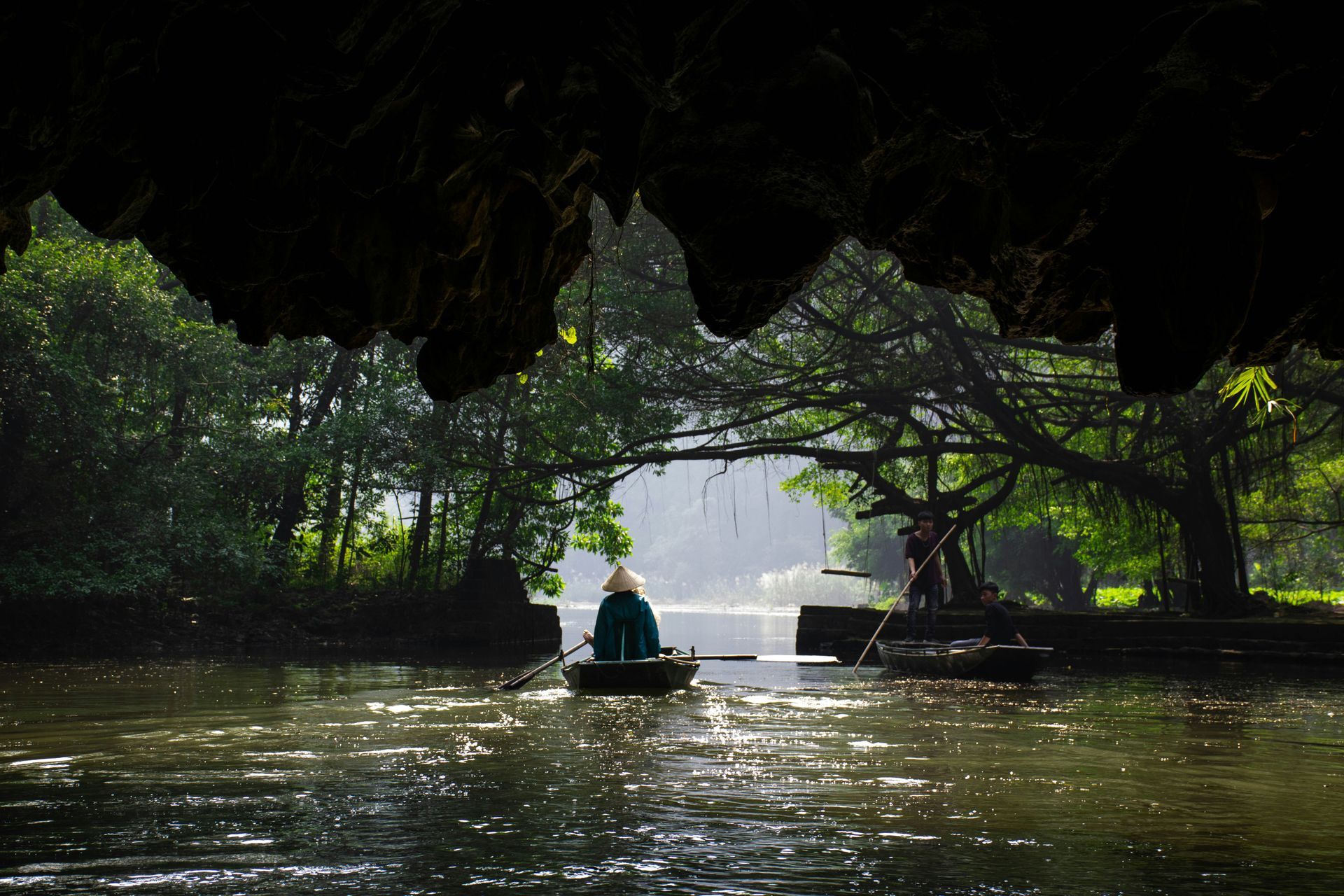 A person rows a boat on a river, visible from a cave opening in Ninh Bình, Vietnam.
