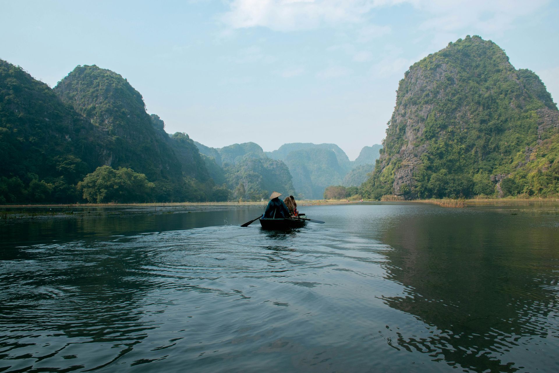 Boat on a river between lush mountains; people rowing in Ninh Bình, Vietnam.