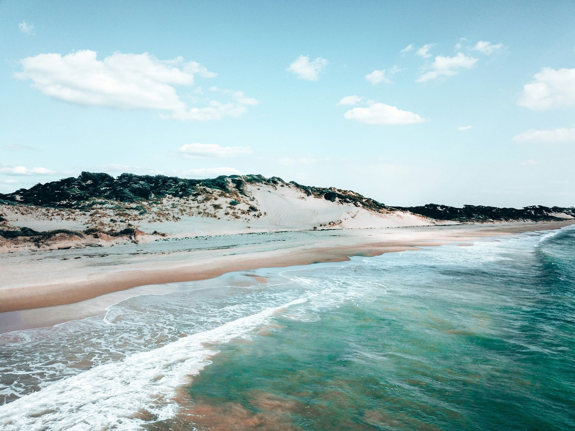An aerial view of a beach with waves crashing on the shore in Western Australia.
