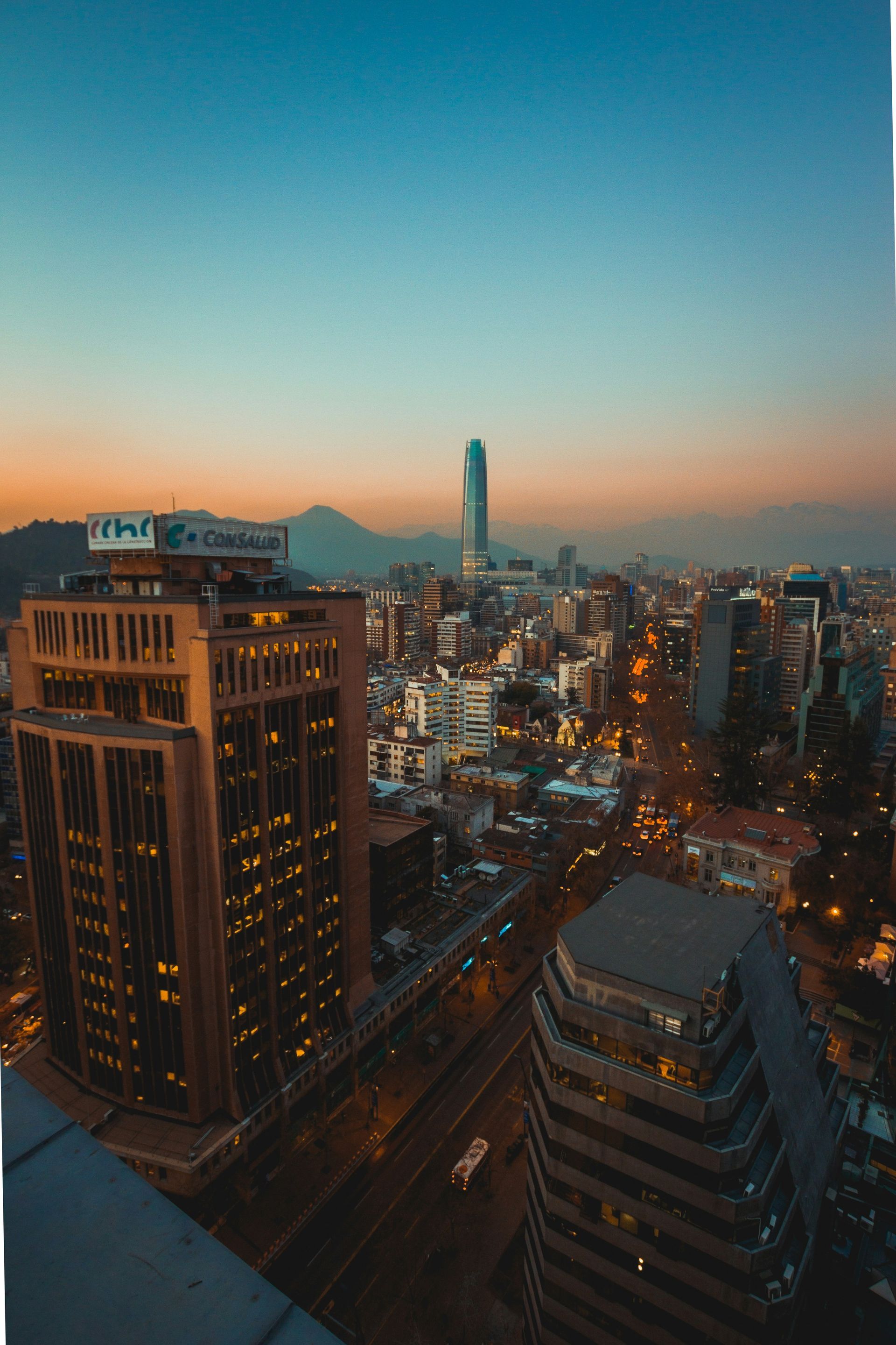 Santiago, Chile skyline at dusk, featuring a mountain backdrop and illuminated buildings with a vibrant orange and blue sky.