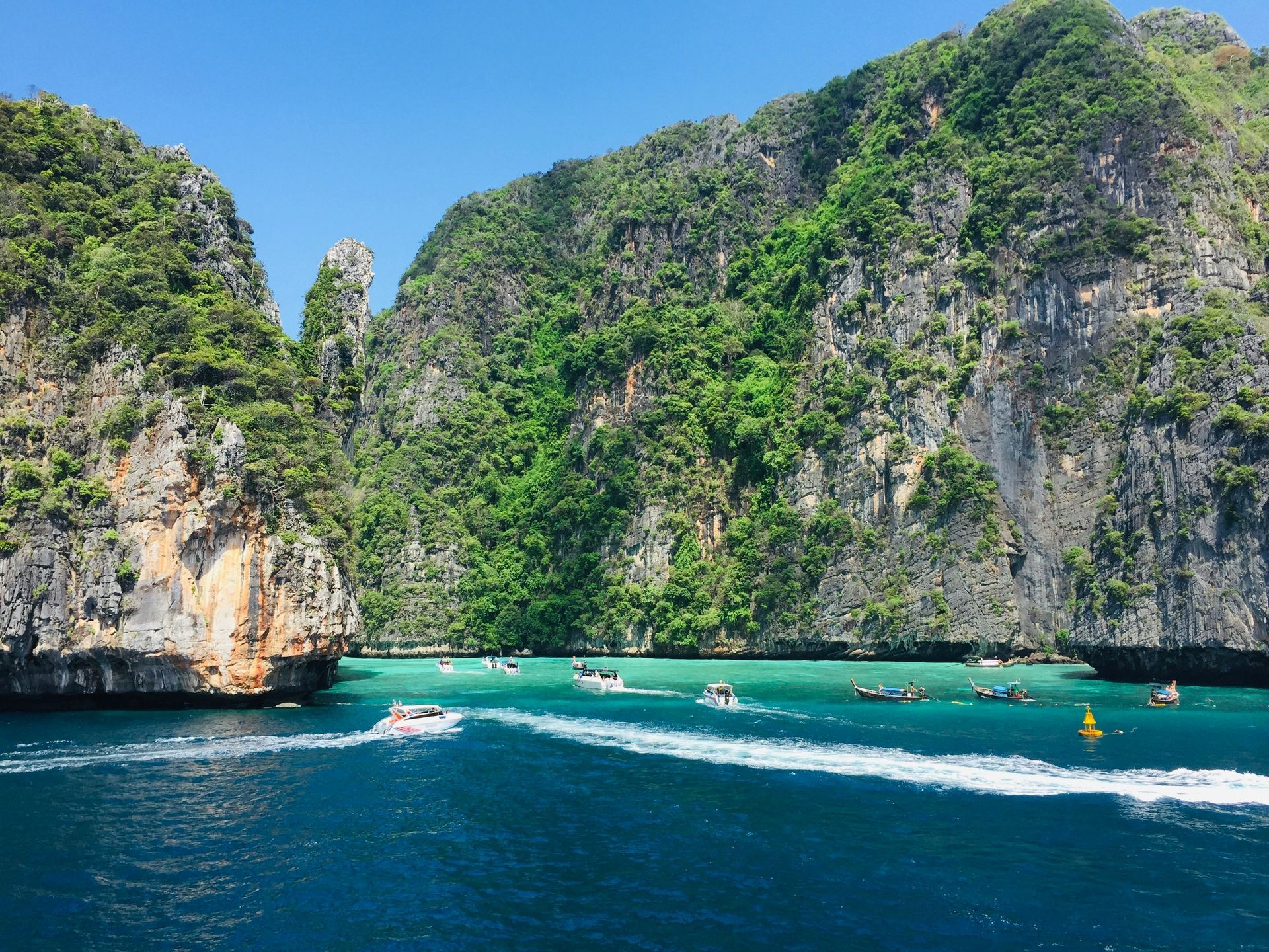 A group of boats are floating on top of a body of water surrounded by the Phi Phi Islands in Krabi, Thailand.