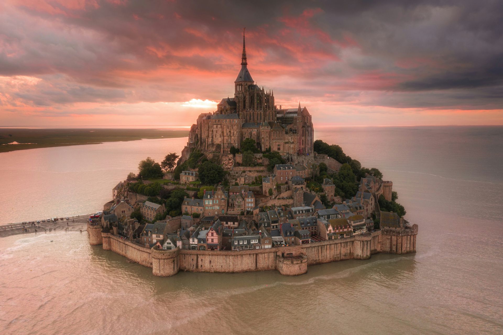 An aerial view of a small island with Mont Saint-Michel on top in the middle of the ocean in Normandy, France.