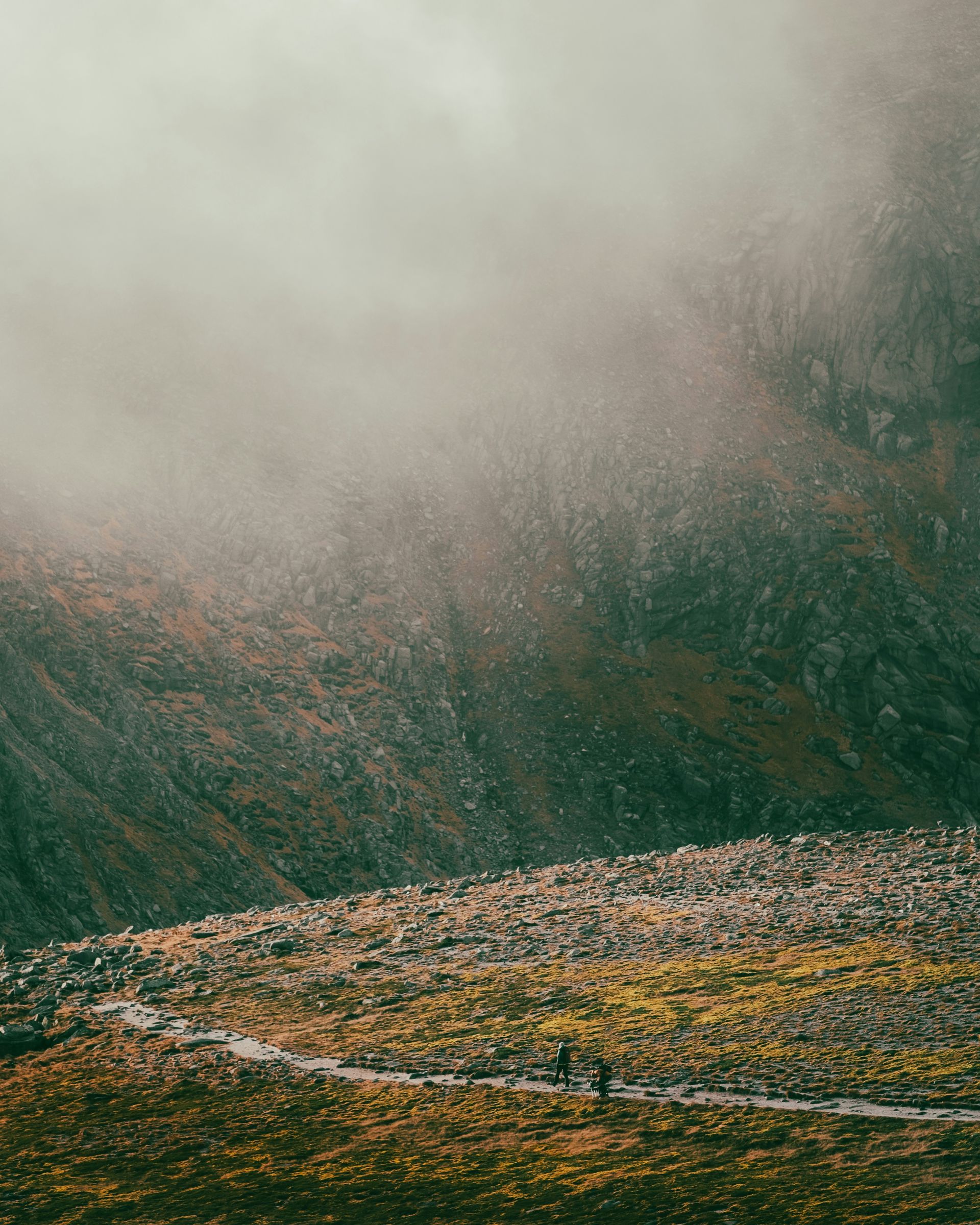 Rocky mountain slope with fog and hints of yellow and green vegetation in Cairngorms National Park, Scotland.