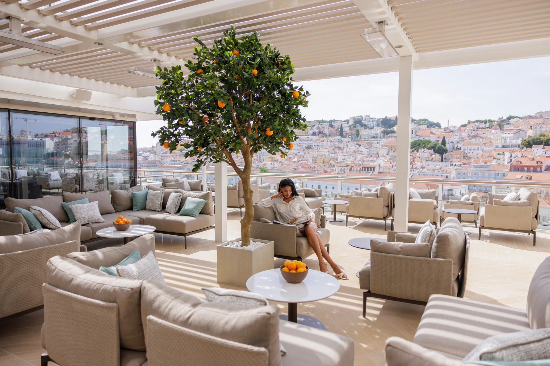 A woman is sitting on a couch under a tree on a patio on Silversea's Silver Ray cruise ship