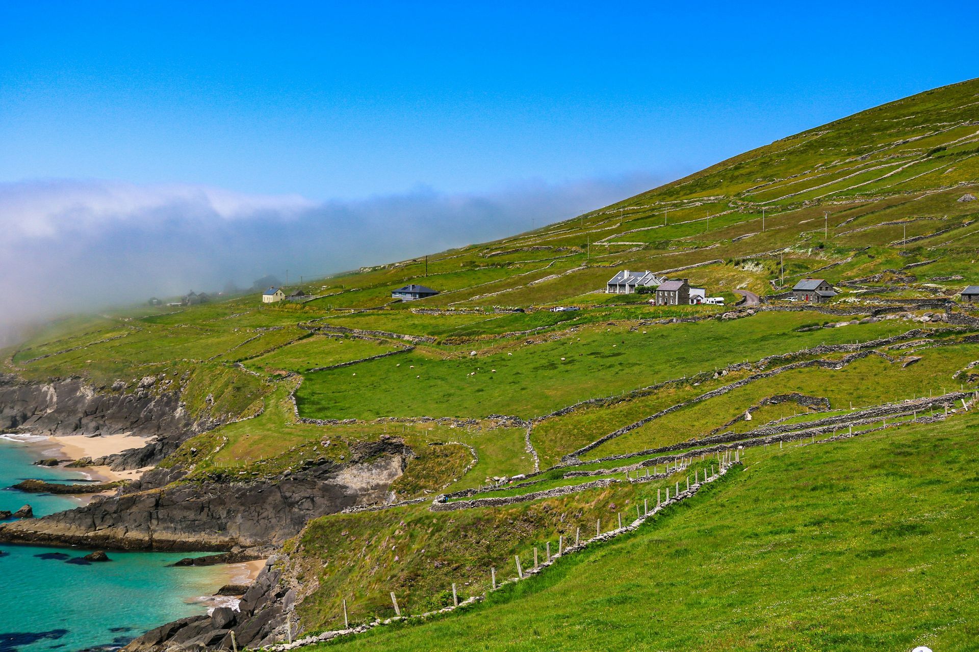 Green hillside village overlooking a turquoise bay on the Dingle Peninsula, Ireland.