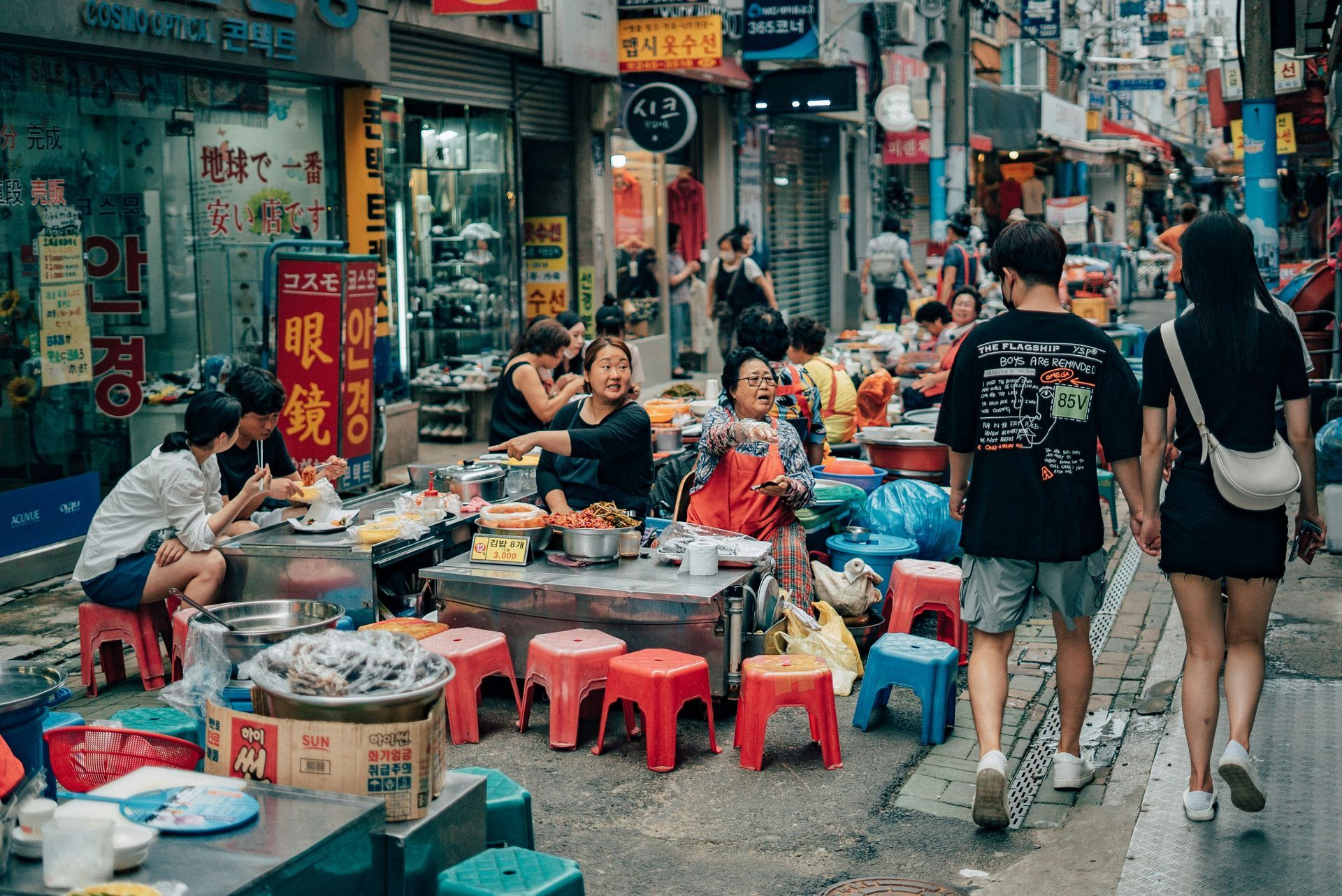 Street food stalls bustling in a narrow street, people eating and walking by in Busan, South Korea.