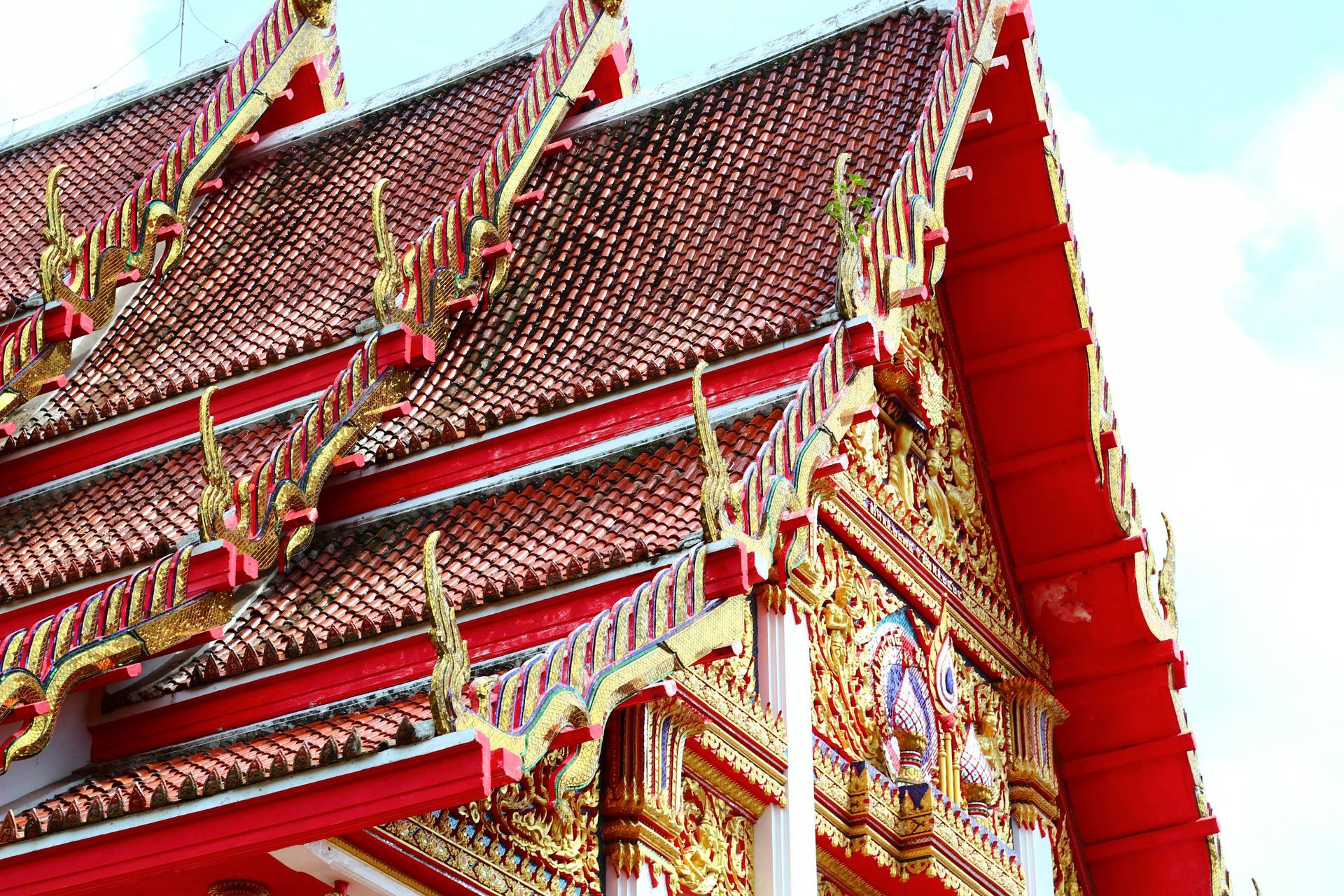 A red and gold roof of a building with a blue sky in the background. in Phuket, Thailand.