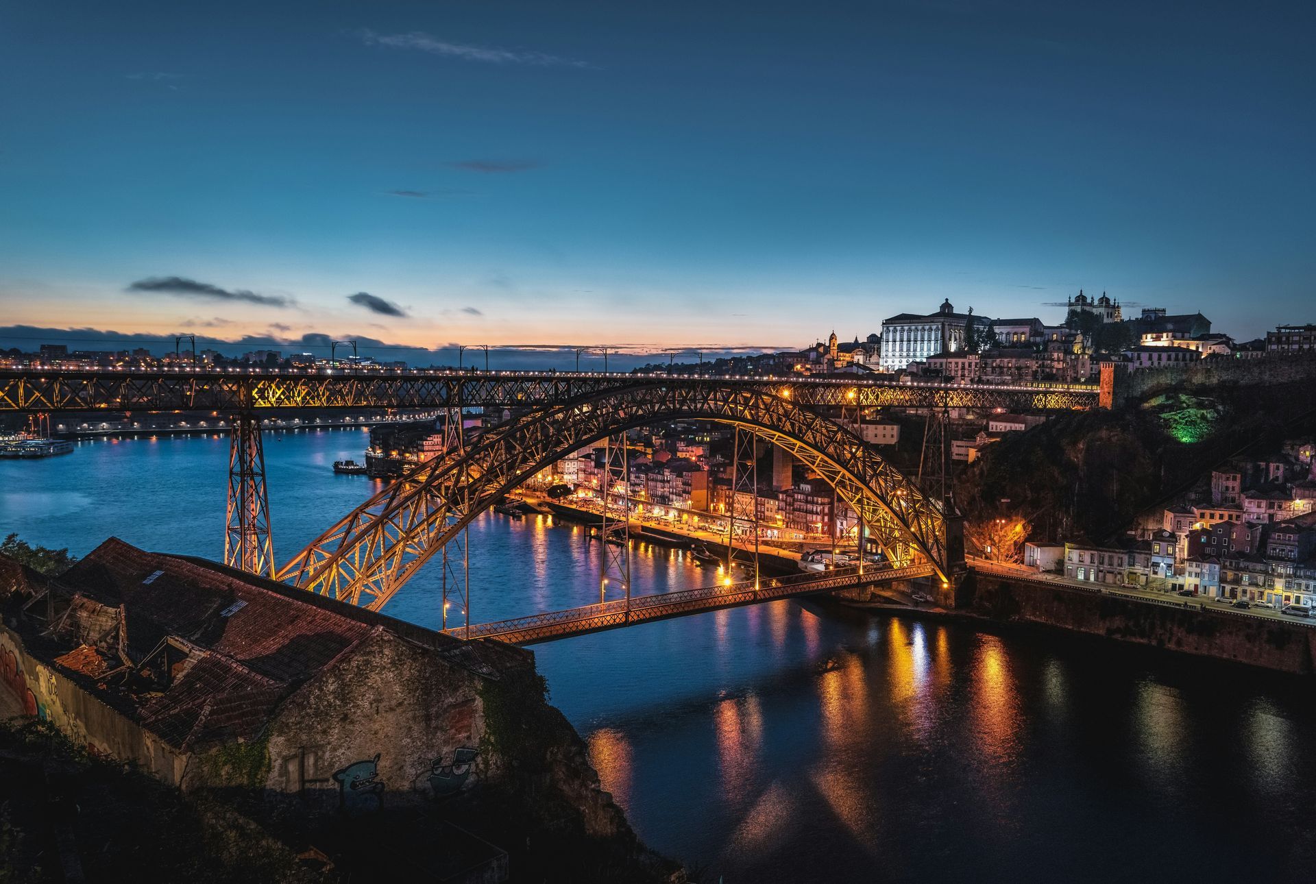 Night view of Dom Luís I Bridge in Porto, Portugal, illuminated with colorful lights over Douro River.