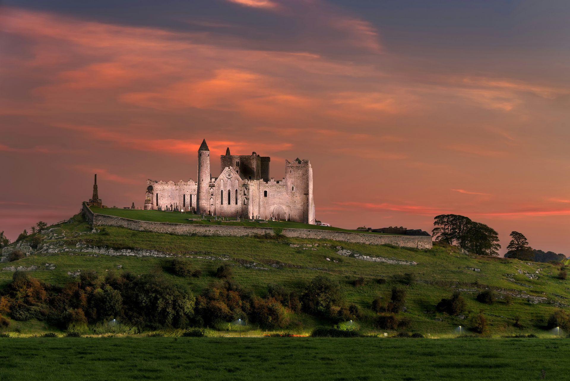 Ruined castle atop a green hill with a sunset sky at the Rock of Cashel, Ireland.