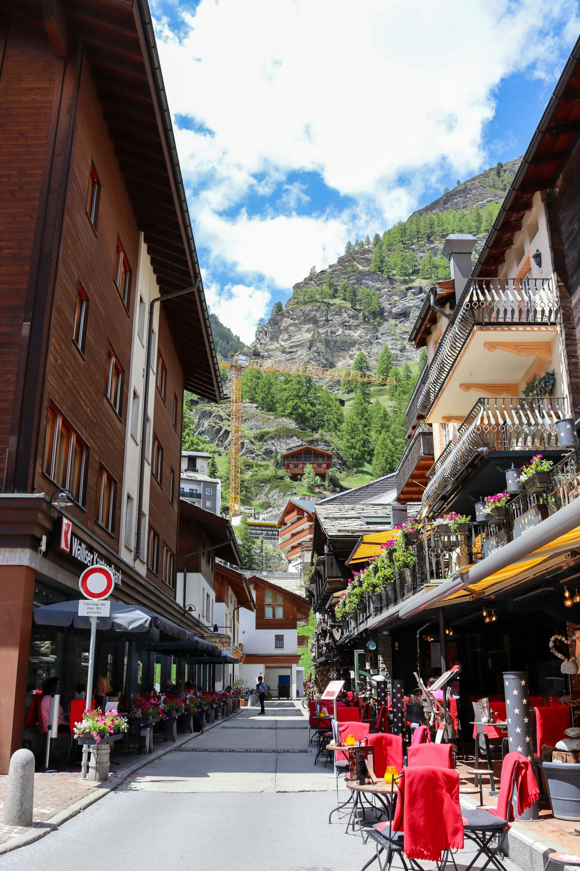 Street in Zermatt, Switzerland, lined with wooden buildings and restaurants; mountain in background.