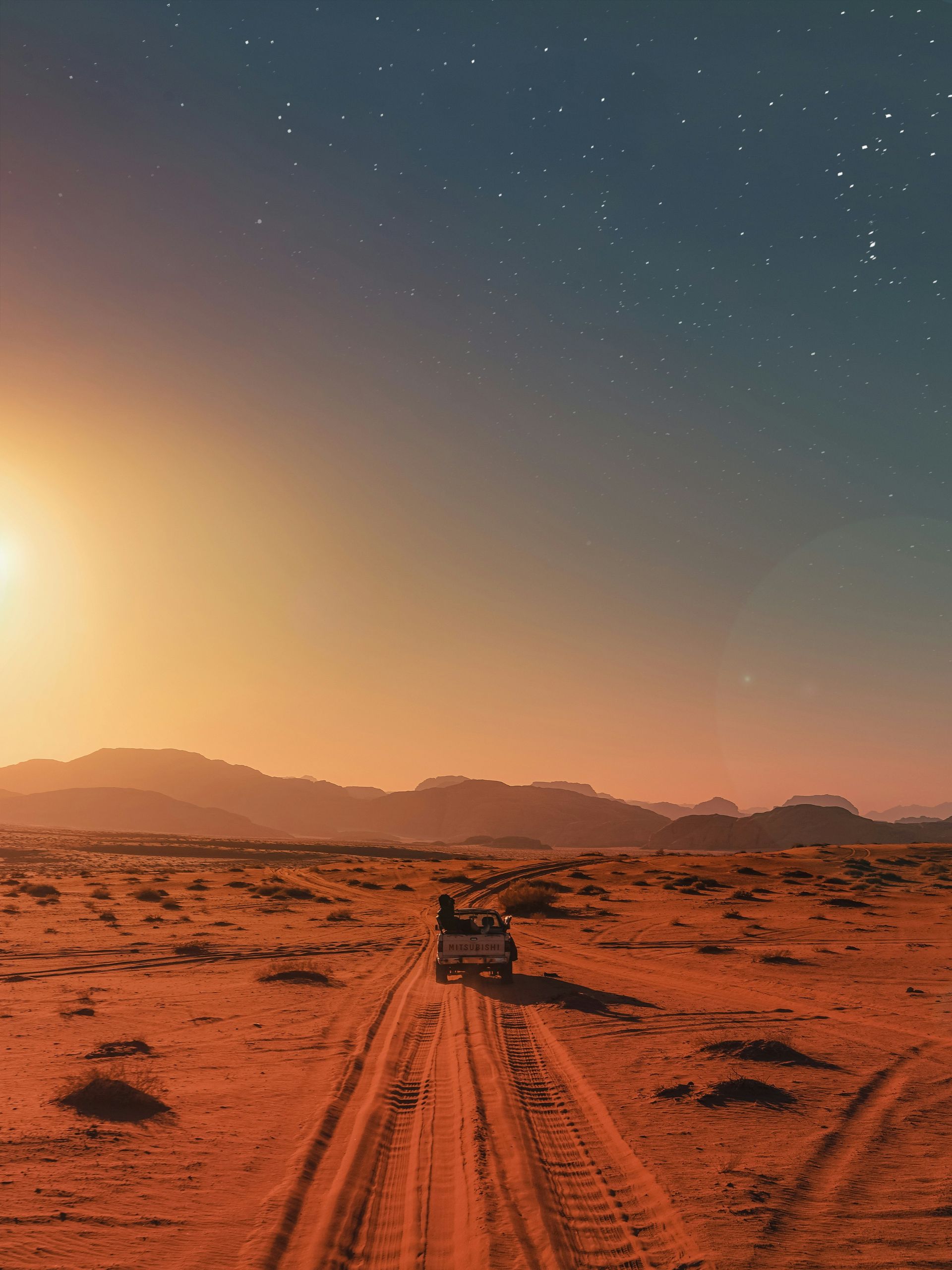 Desert landscape with car driving on dirt road under a starry night sky in Wadi Rum, Jordan.