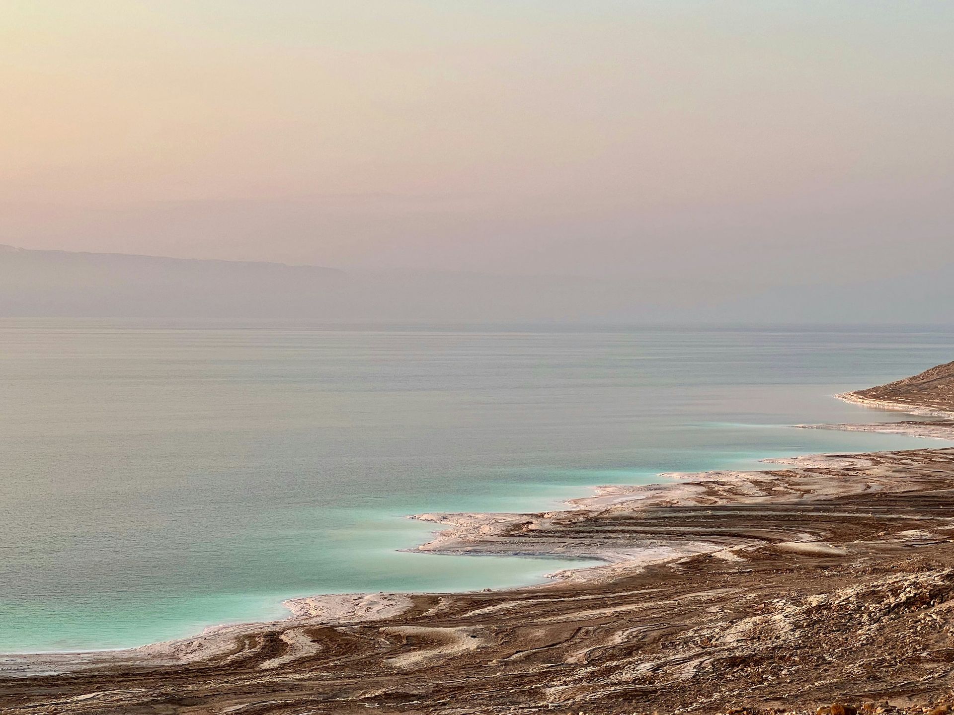 A scenic view of the Dead Sea with light blue water and a shoreline of white salt deposits in Jordan.