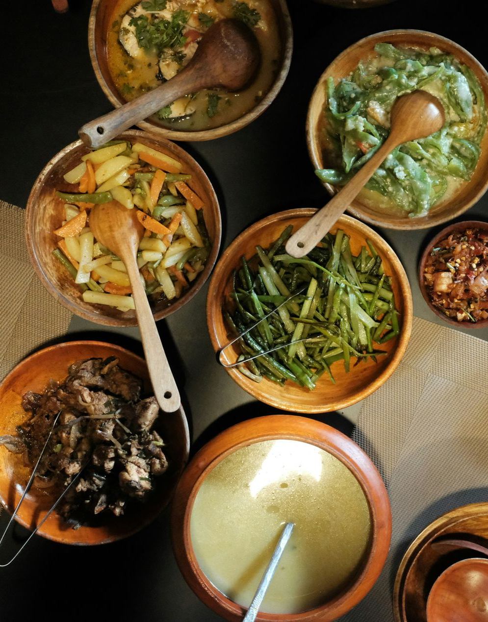 Overhead view of several wooden bowls filled with various Bhutanese foods, each with a wooden spoon.
