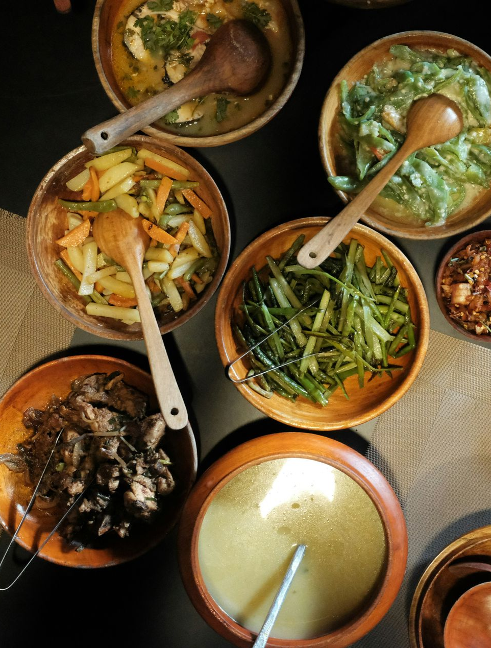 Overhead view of several wooden bowls filled with various Bhutanese foods, each with a wooden spoon.