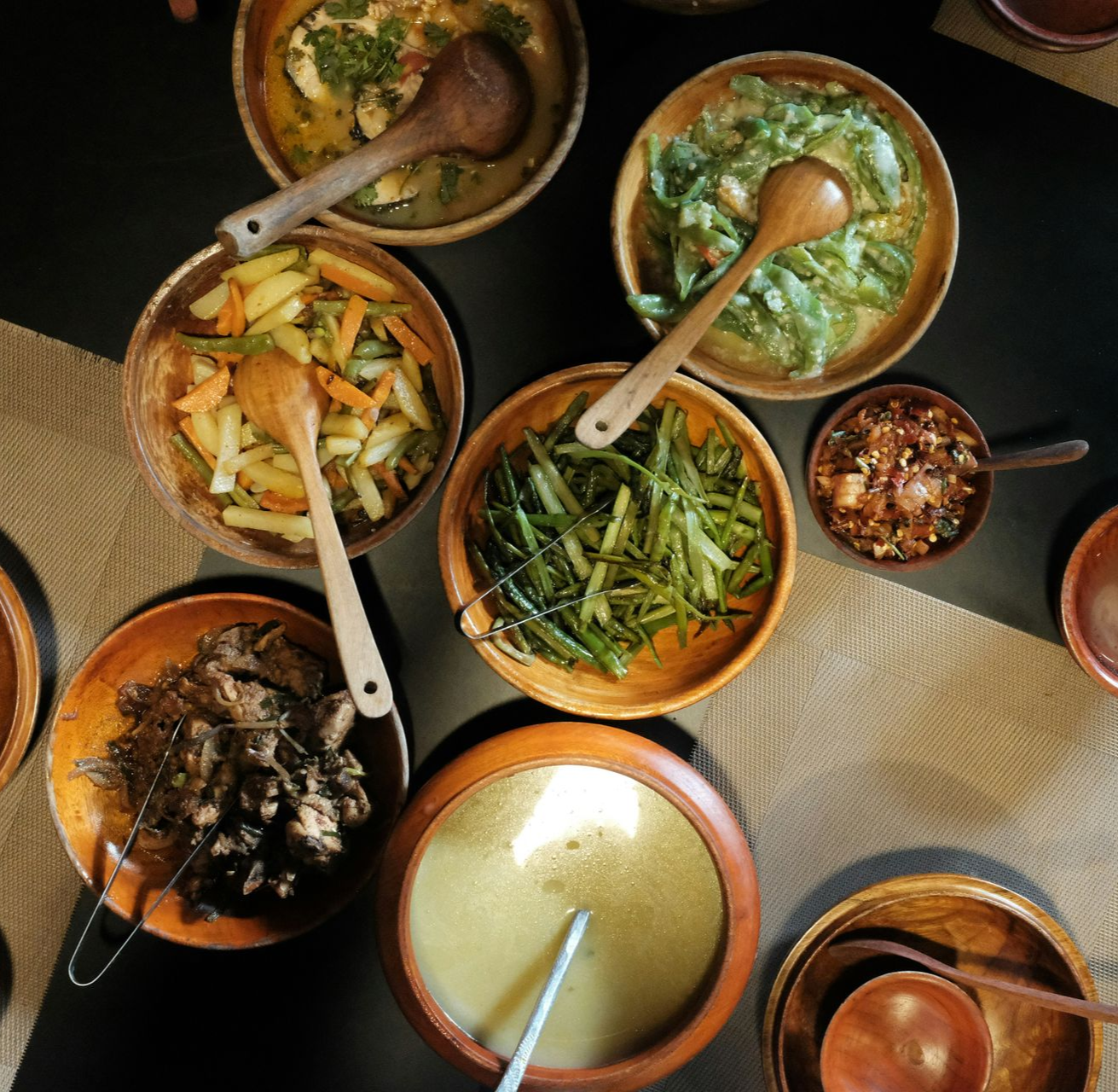 Overhead view of several wooden bowls filled with various Bhutanese foods, each with a wooden spoon.