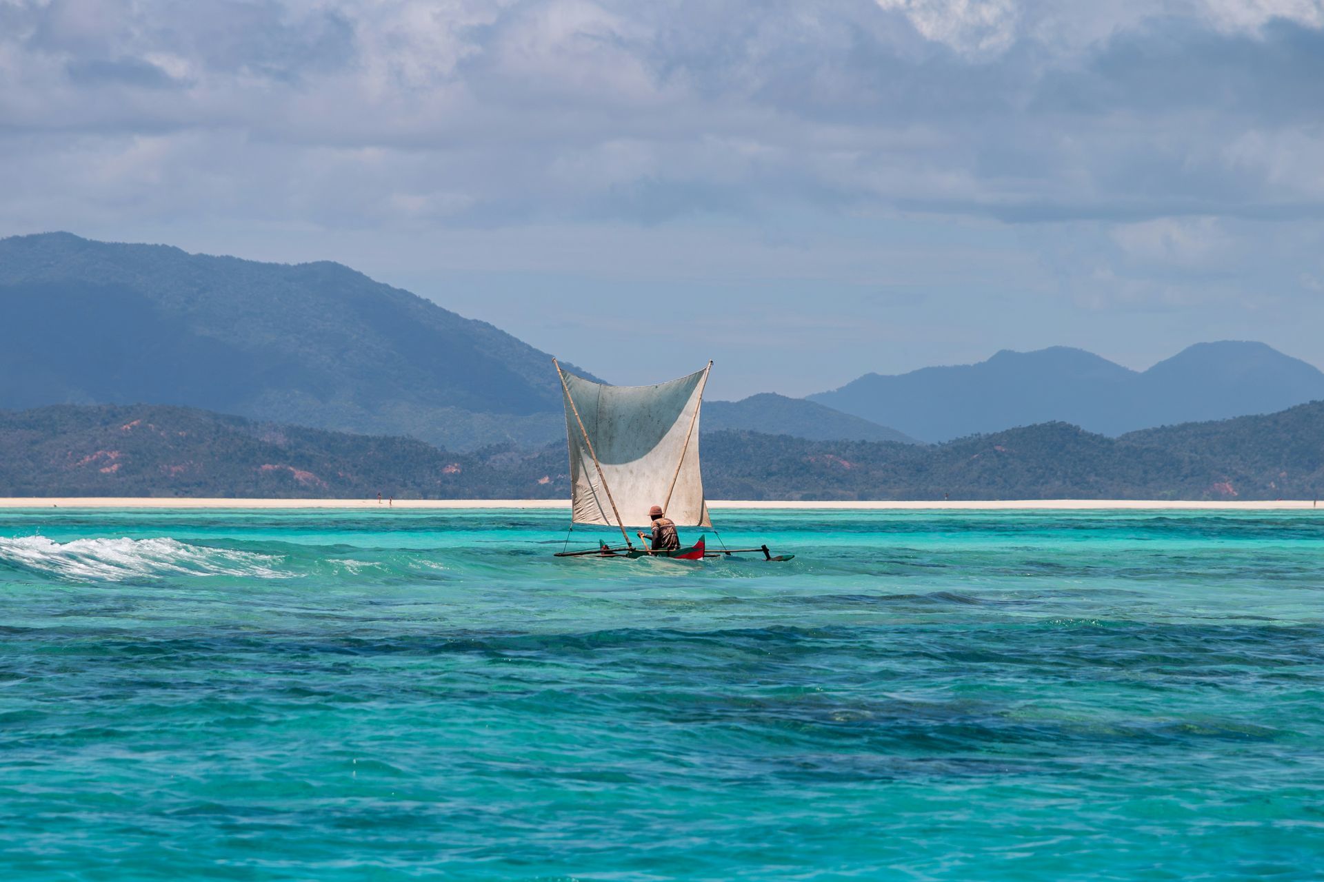Sailboat on turquoise water, mountains in the background on Nosy Iranj, Madagascar.