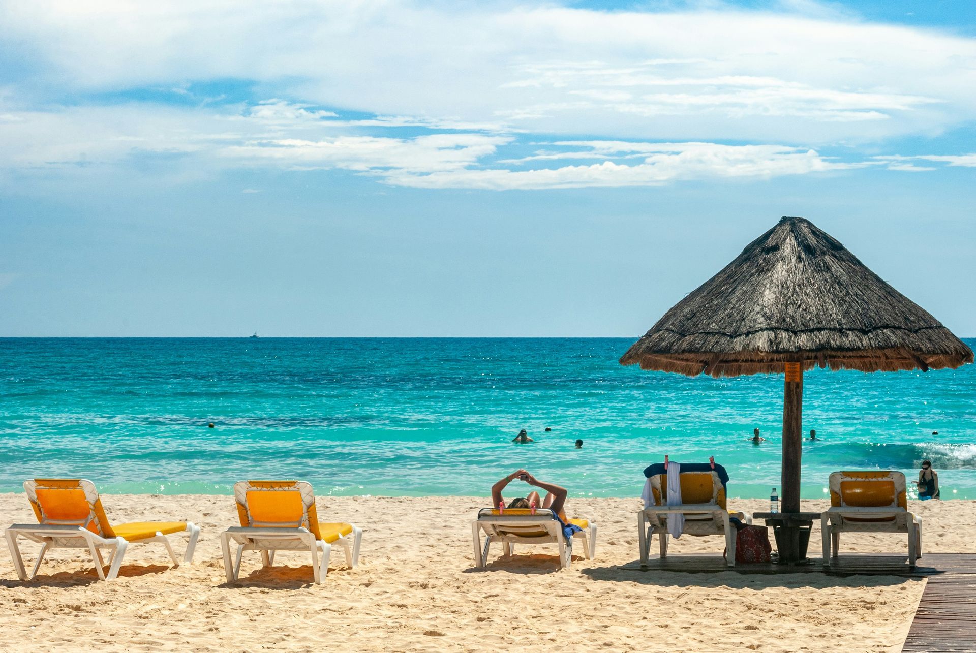 Beach scene with turquoise water, white sand, and yellow lounge chairs under a thatched umbrella in Cancún, Mexico.
