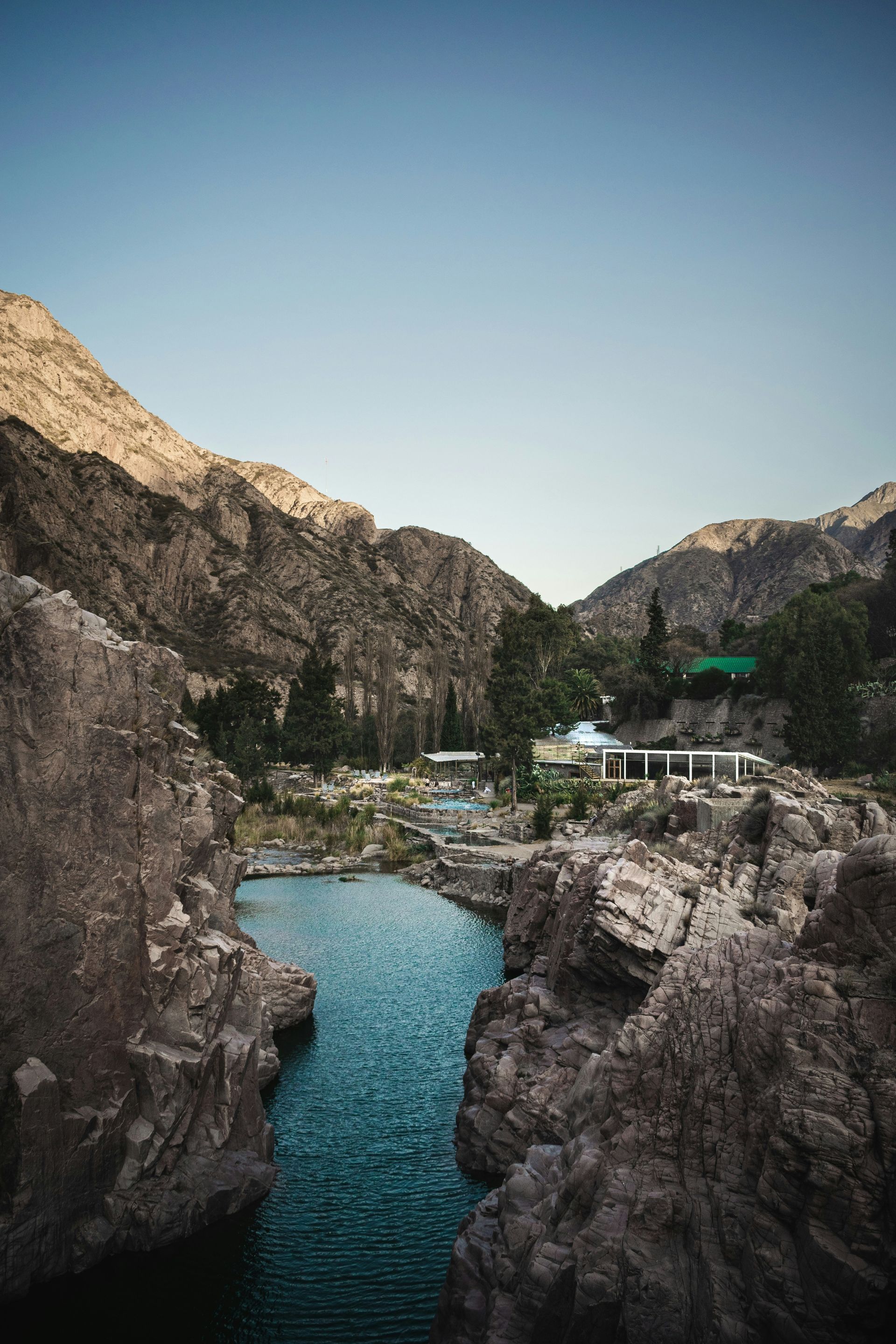 Rocky canyon with blue water, buildings, and a clear sky in Mendoza, Argentina.