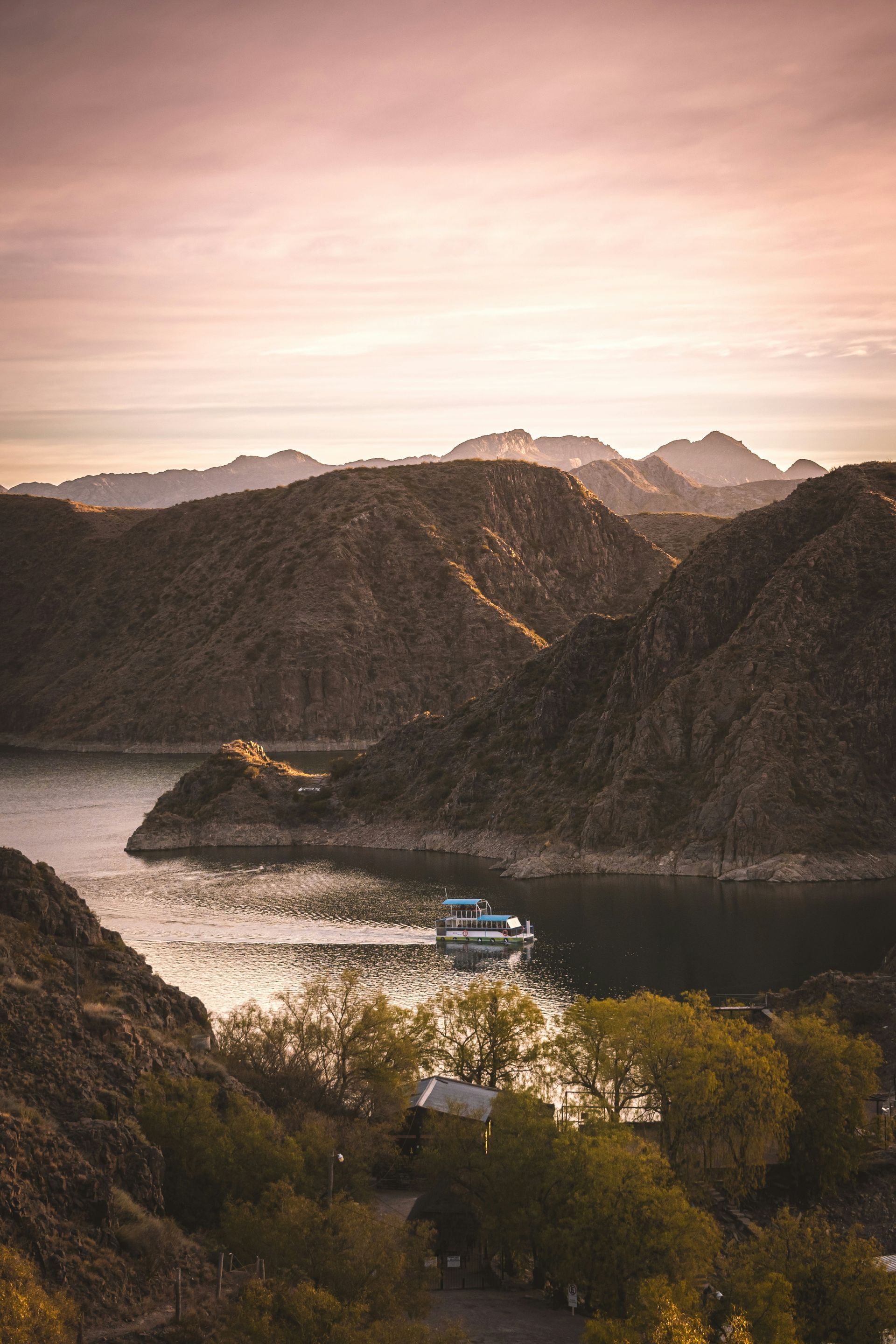 Boat on calm water, surrounded by rugged mountains under a pink and orange sunset in Mendoza, Argentina.