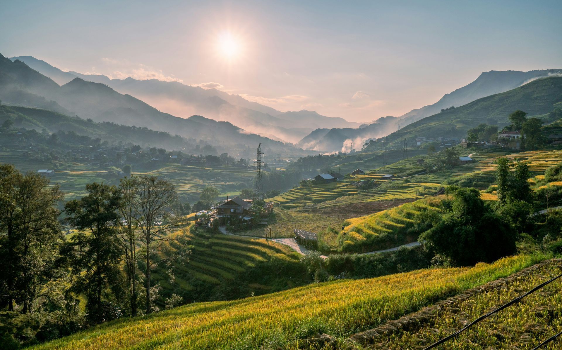 Sunlit mountain valley with terraced rice fields, houses, and hazy mountains in Sapa, Vietnam. 