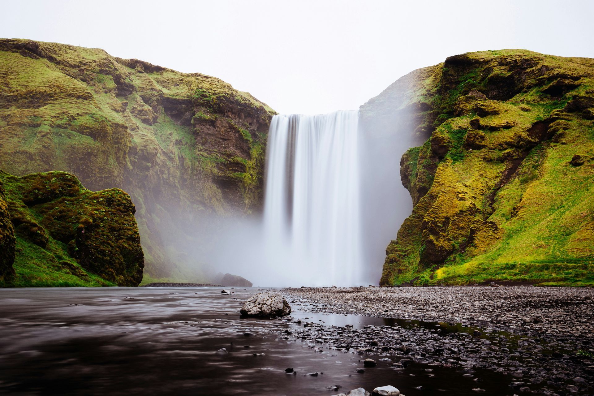 Skógafoss Waterfall cascading down into a misty pool, flanked by mossy green cliffs in Iceland.
