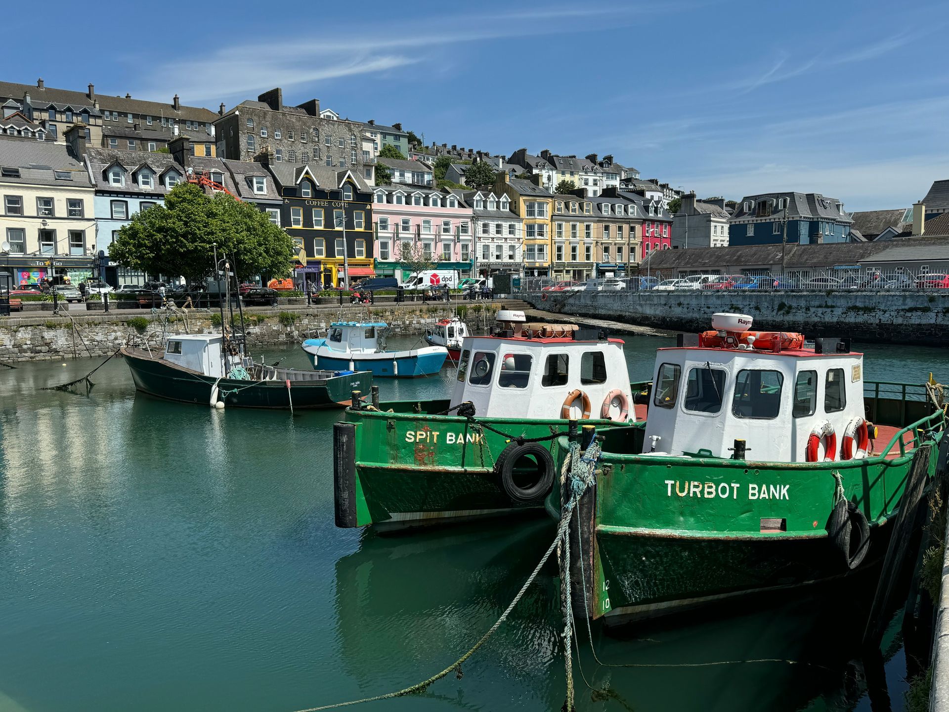 Boats docked in harbor, colorful buildings on hillside in Cork, Ireland.