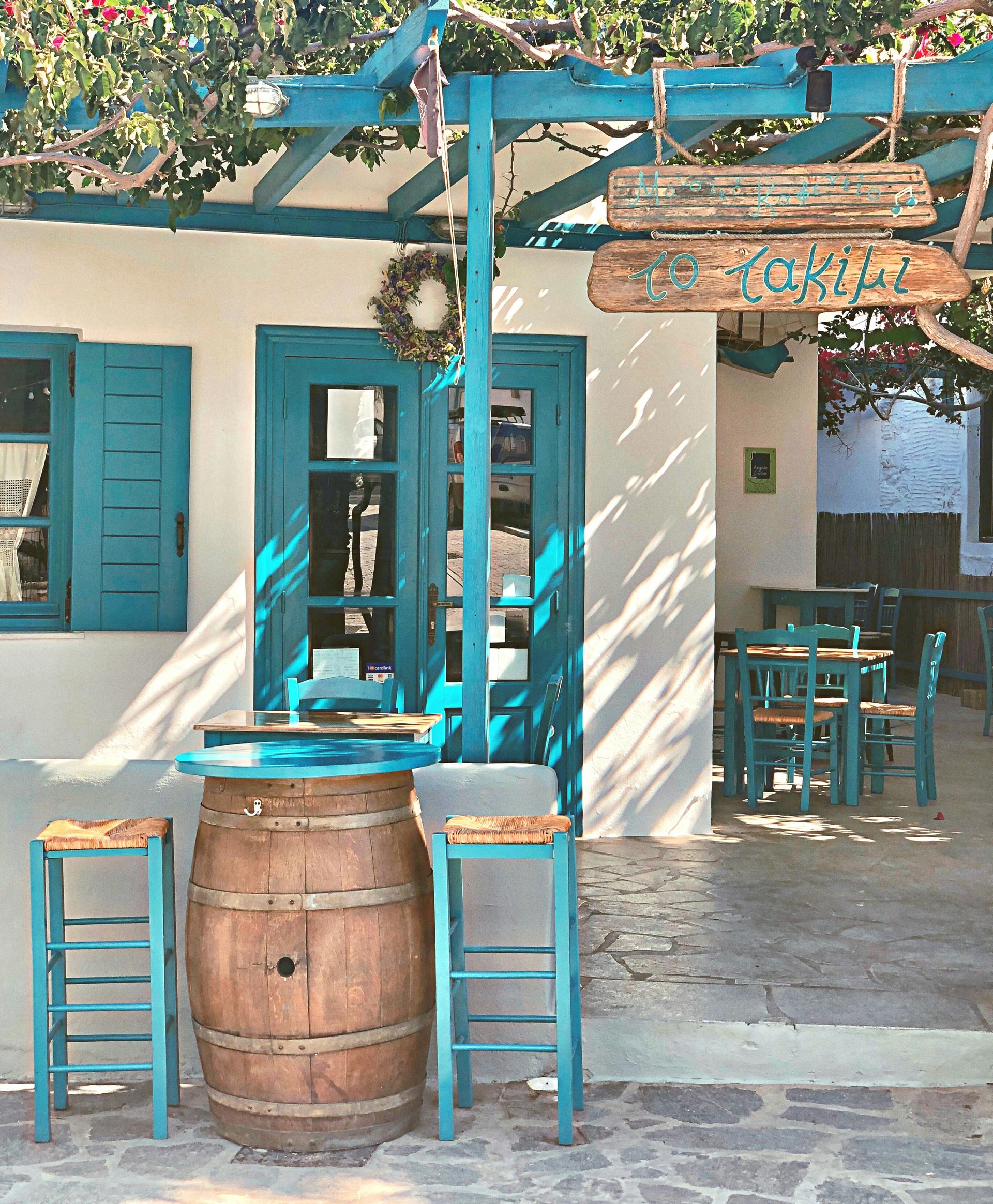 A wooden barrel sits in front of a white building with blue shutters in Paros, Greece.