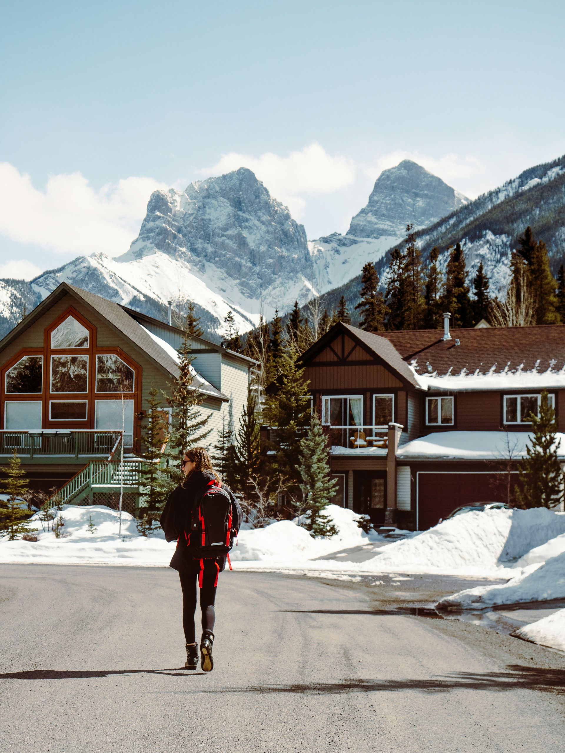 Person walking towards houses with snowy mountains in the background in Canmore, Canada.