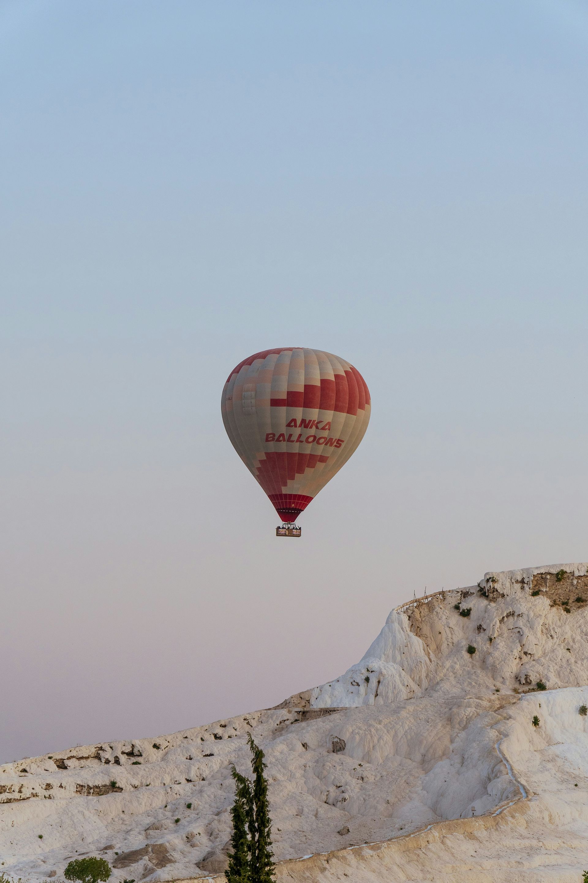 Hot air balloon with red and white design over white rock formations in Pamukkale, Turkey.