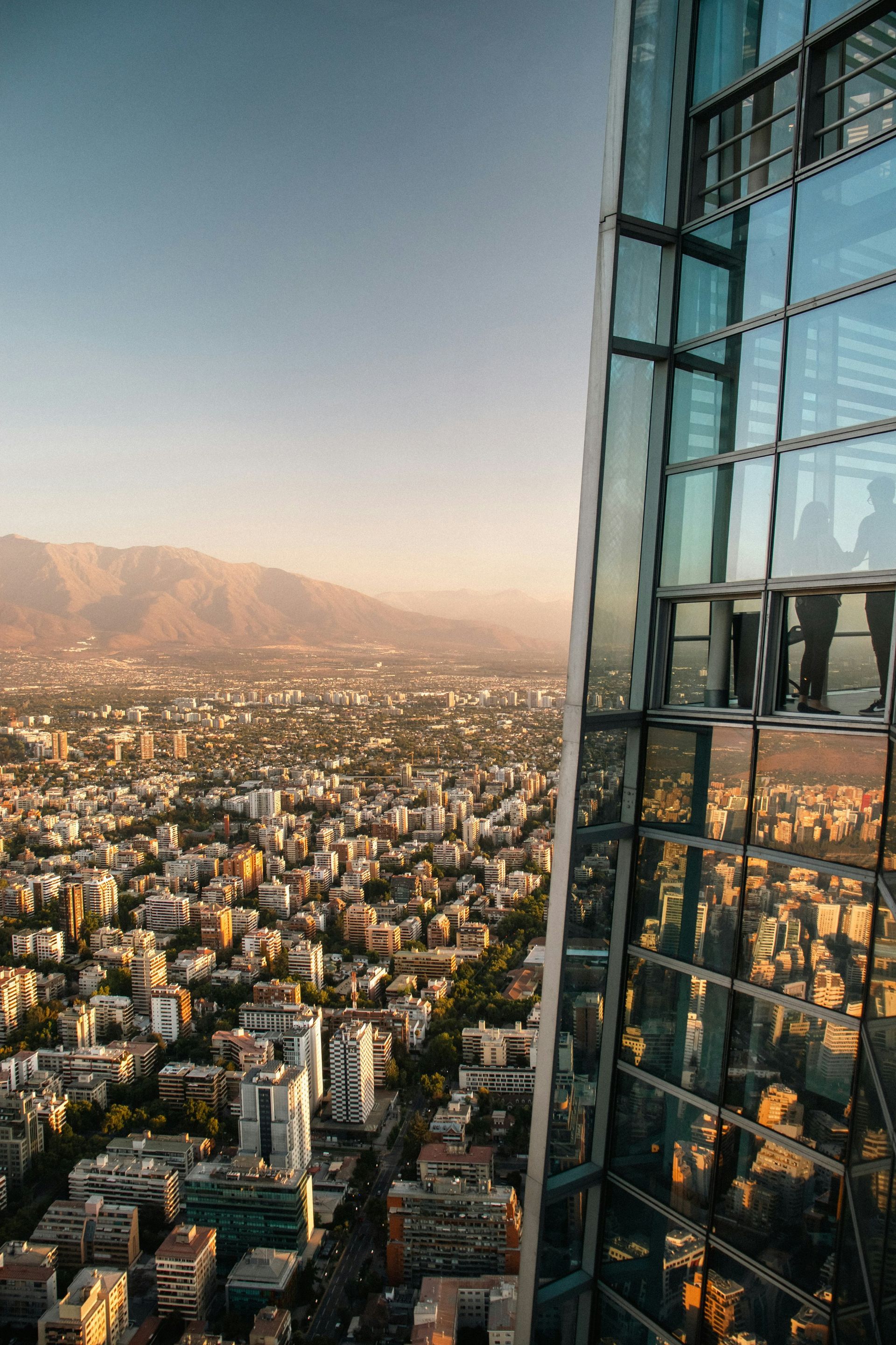Santiago, Chile's skyline view from a tall glass building, showcasing densely packed buildings under a hazy sunset.