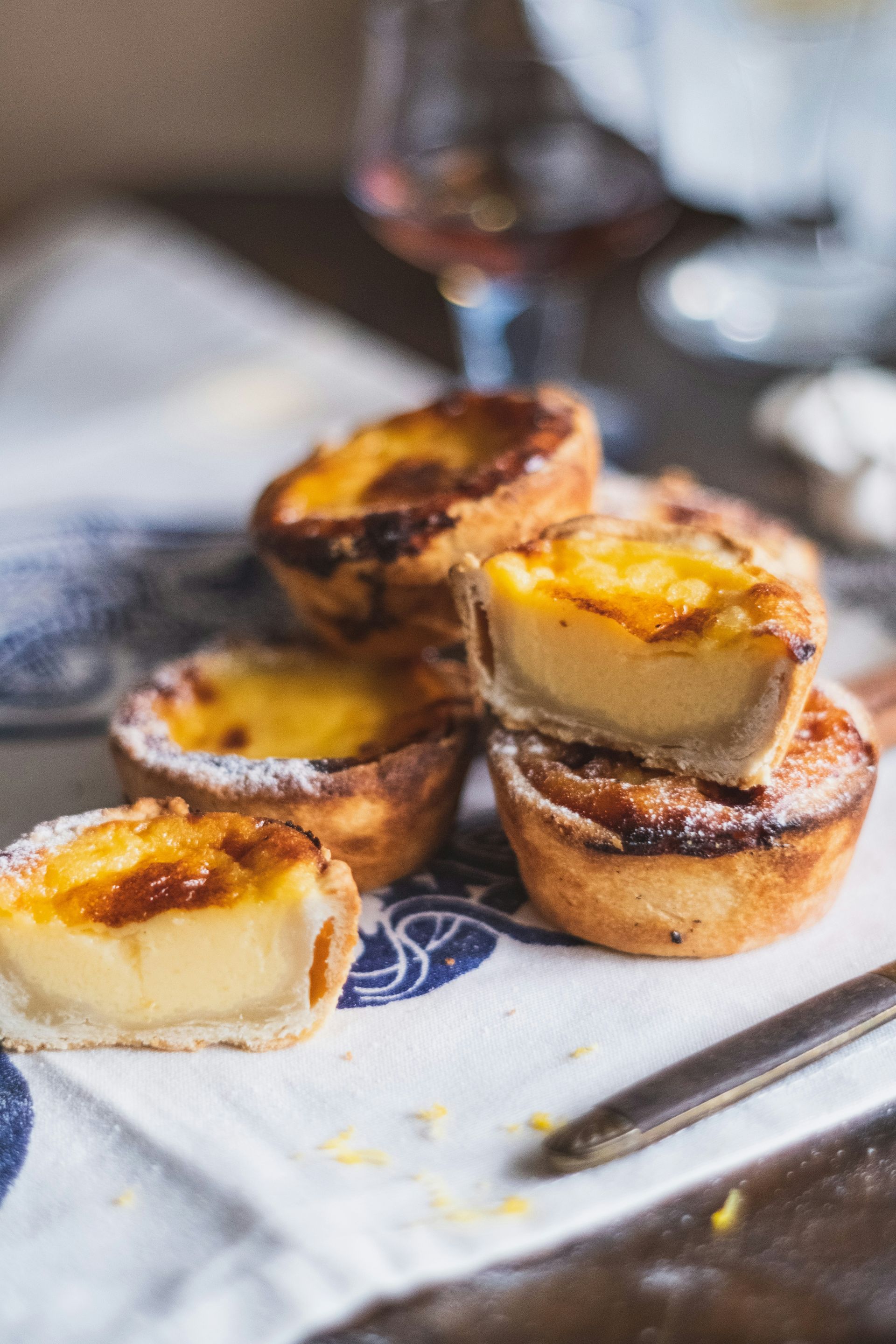 Several Pastel de Natas - crusted Portuguese custard tarts on a patterned cloth.