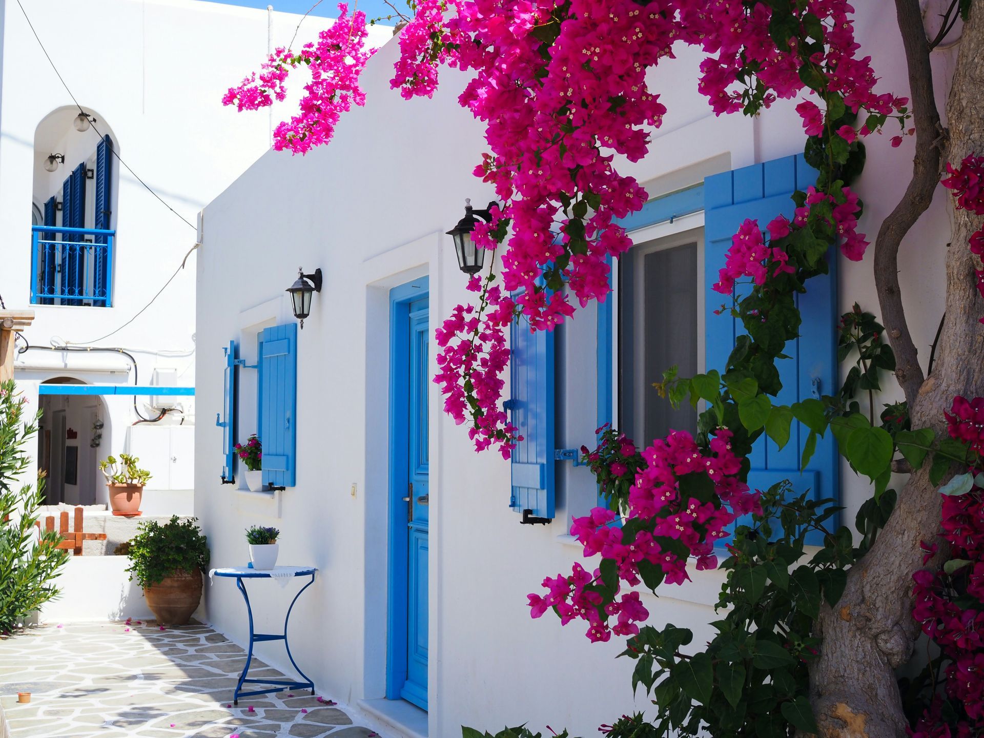 A white building with blue shutters and pink flowers in Mykonos, Greece.