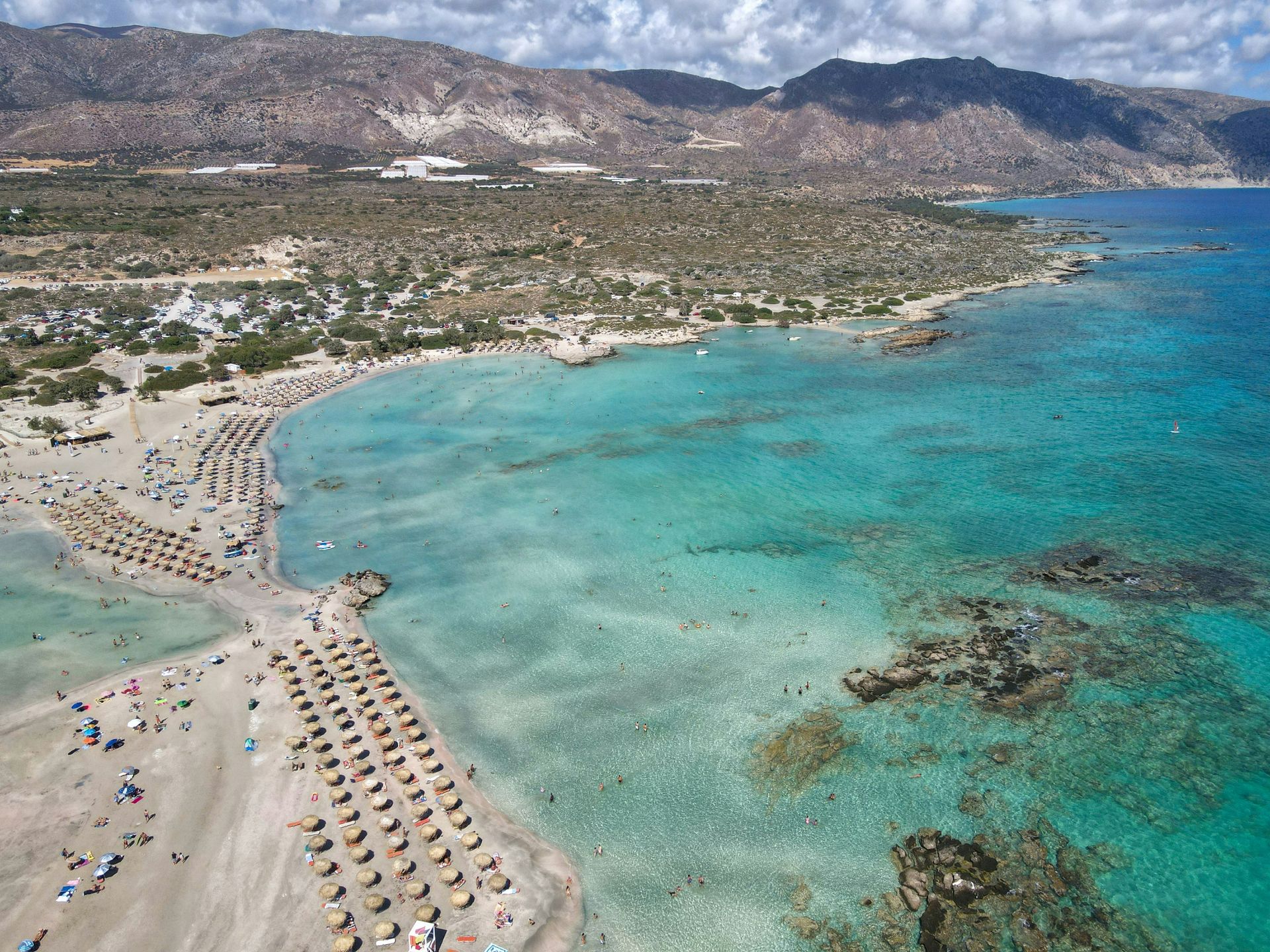 An aerial view of Elafonisi beach with umbrellas and mountains in the background in Crete, Greece.