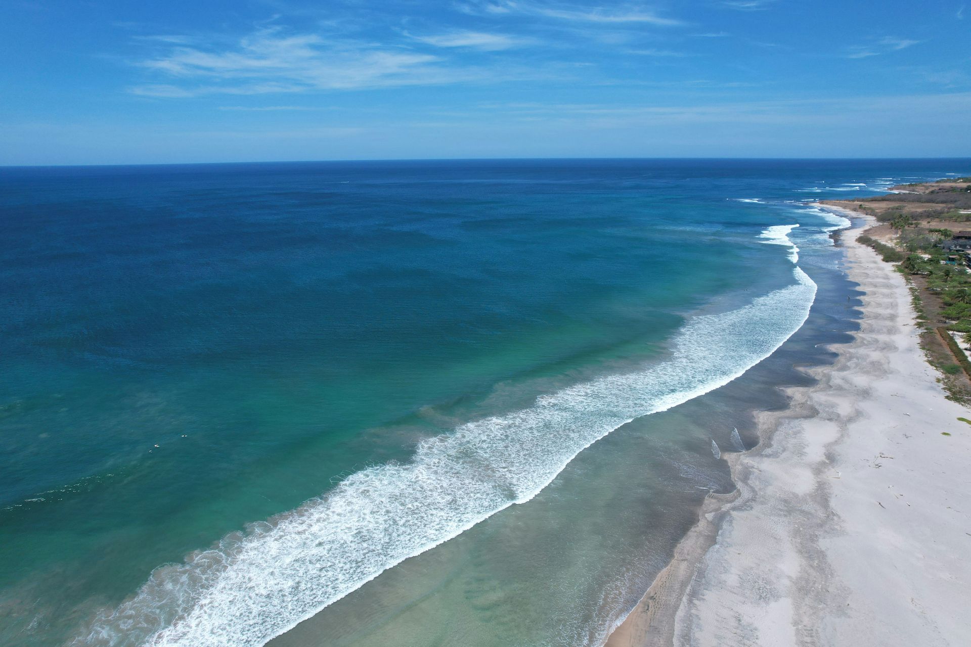 Aerial view of a beach with turquoise water and white waves meeting the shore in Tamarindo, Costa Rica.