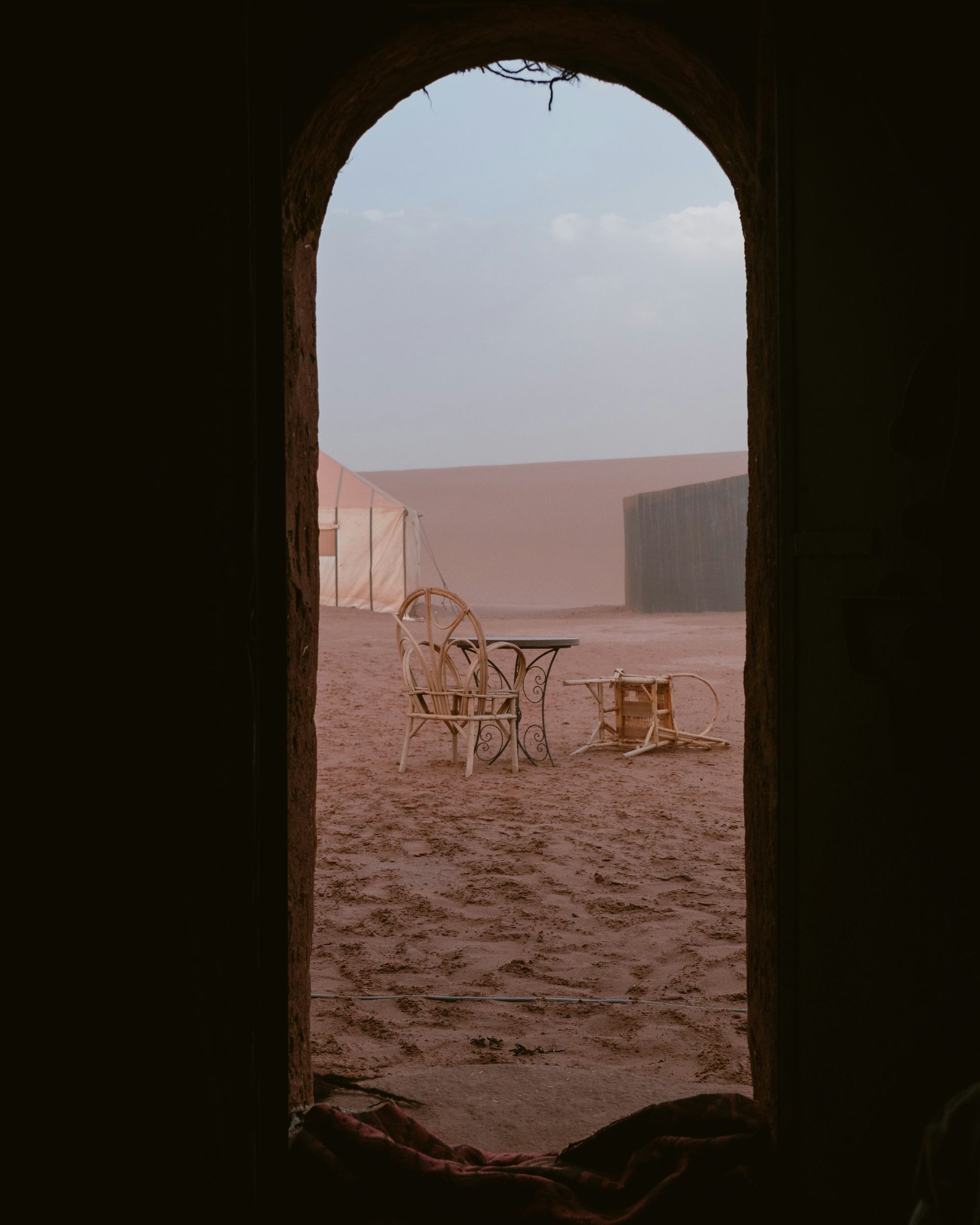 A view of a table and chairs in the desert through an archway in Erg Chebbi, Morocco.