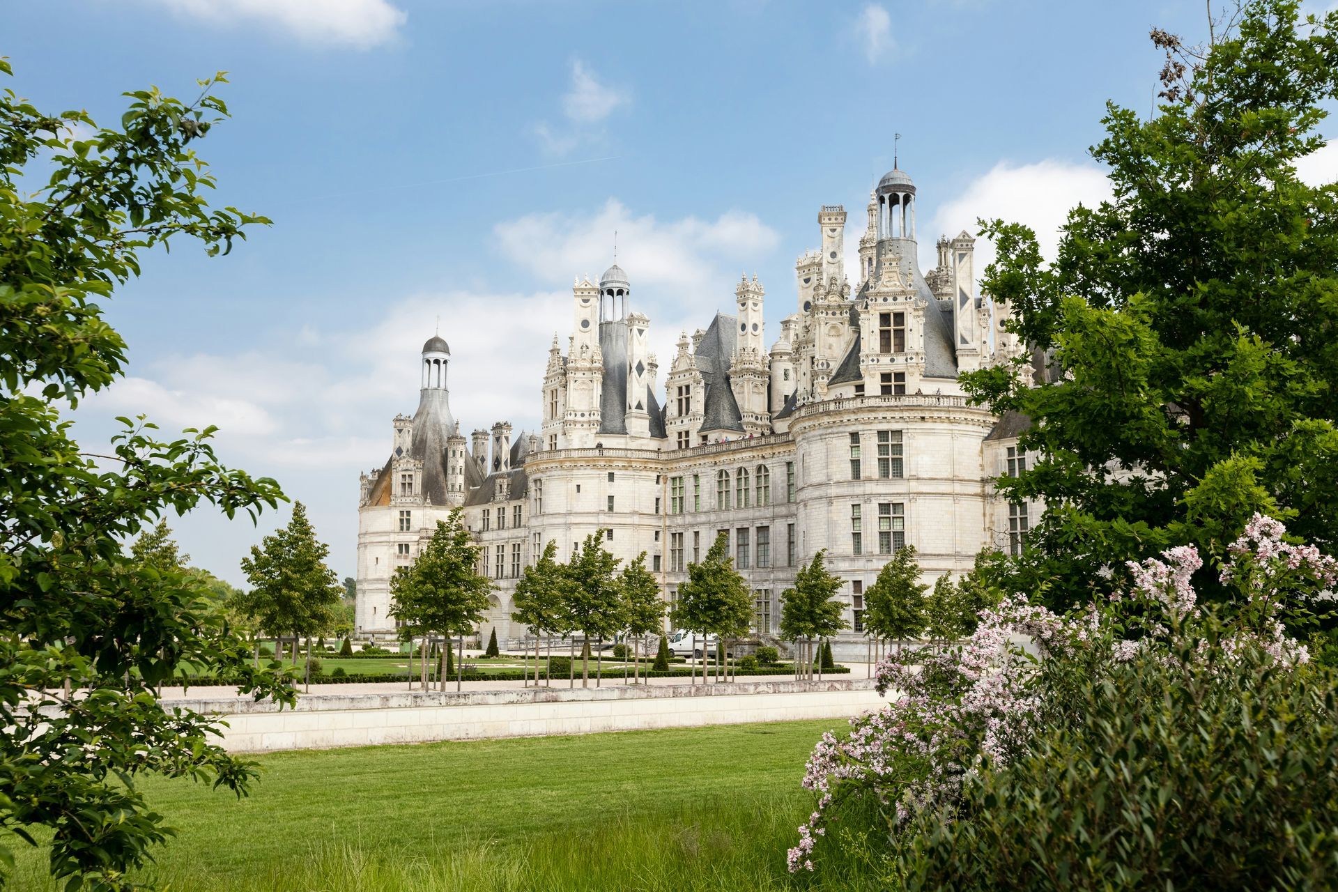 The Château de Chambord is a large white building surrounded by trees and grass in the Loire valley, France.