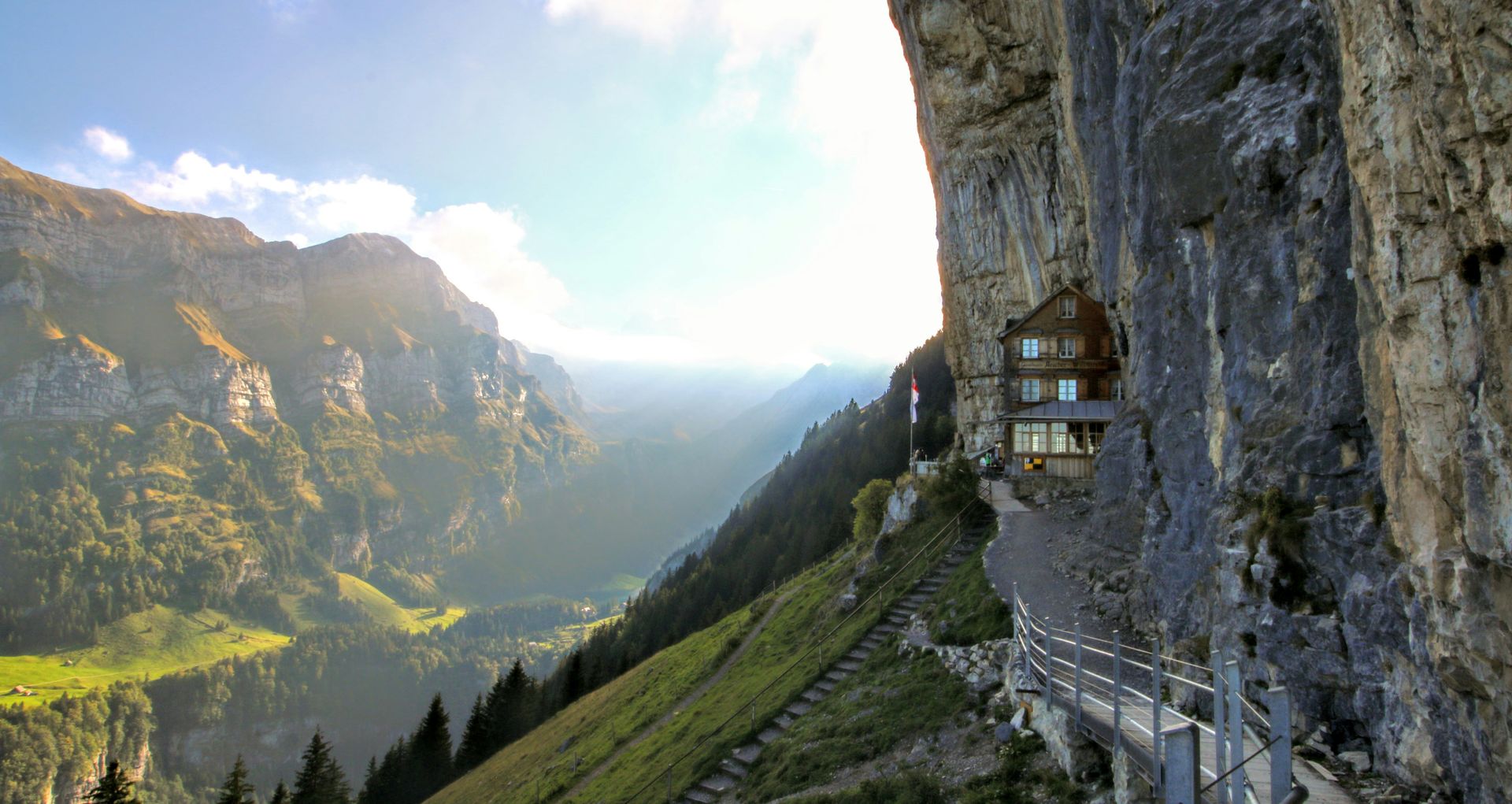 The Aescher house, built into a cliffside in a mountain valley, with a pathway along the rock face in Schwende, Switzerland.